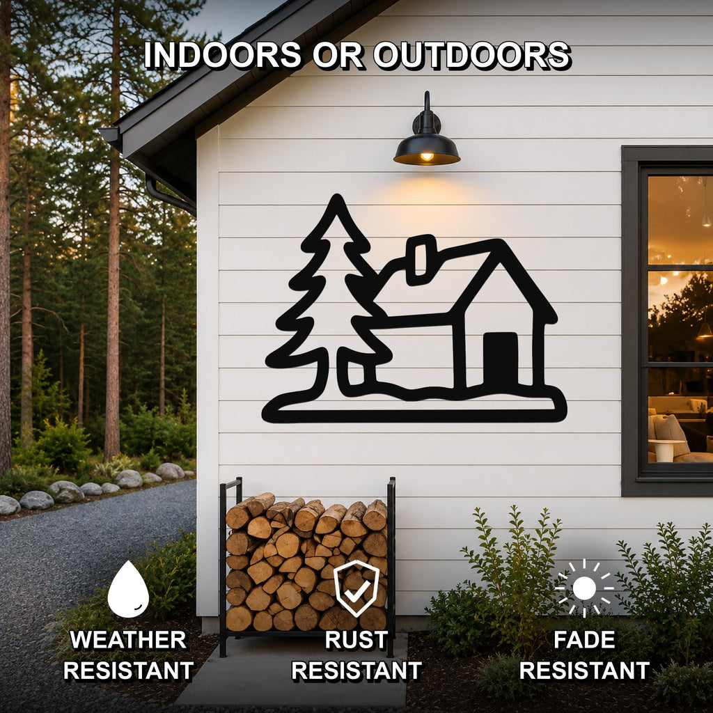 Black metal wall art featuring a cabin and tree silhouette, mounted on a white exterior wall above a firewood rack, weather resistant, rust resistant, and fade resistant.