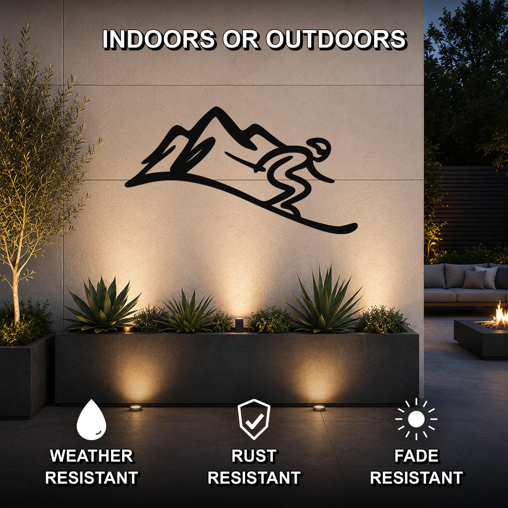 Black metal wall art featuring a skier silhouette on a mountain, mounted on an outdoor wall above a planter with succulents, illuminated by ground lights.