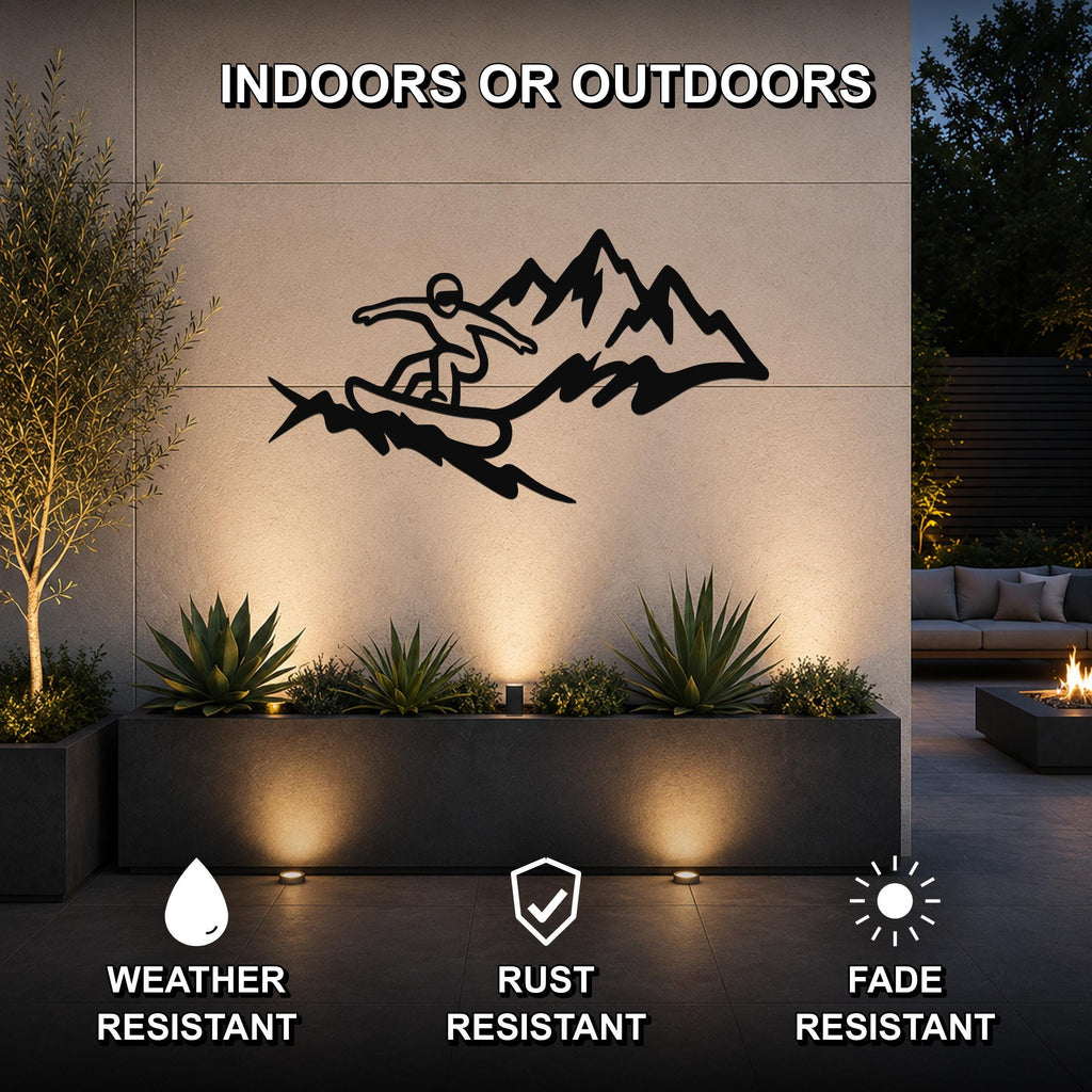 Black metal wall art featuring a snowboarder silhouette in motion against mountain peaks, mounted on an outdoor wall above a planter with accent lighting.