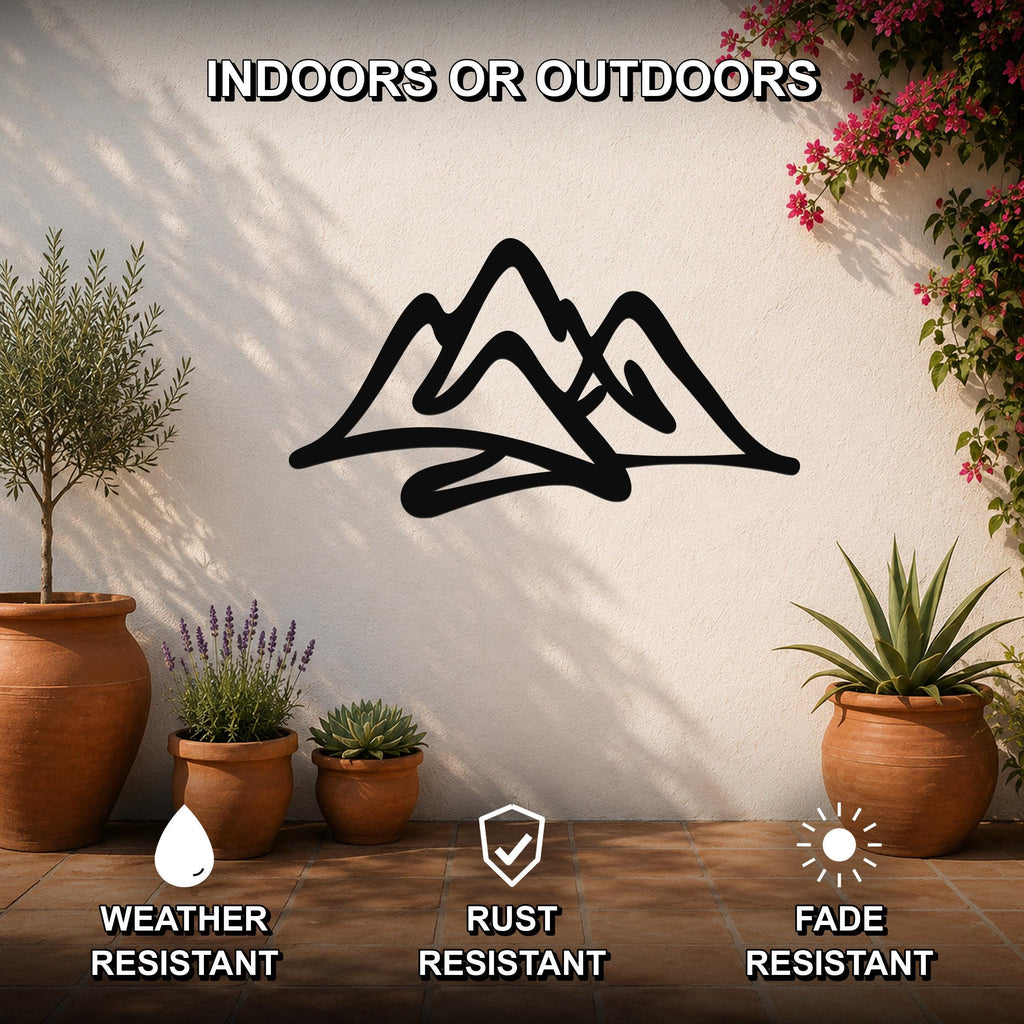 Black metal mountain silhouette wall art with layered peaks, mounted on a white outdoor wall above potted plants on a tiled patio.
