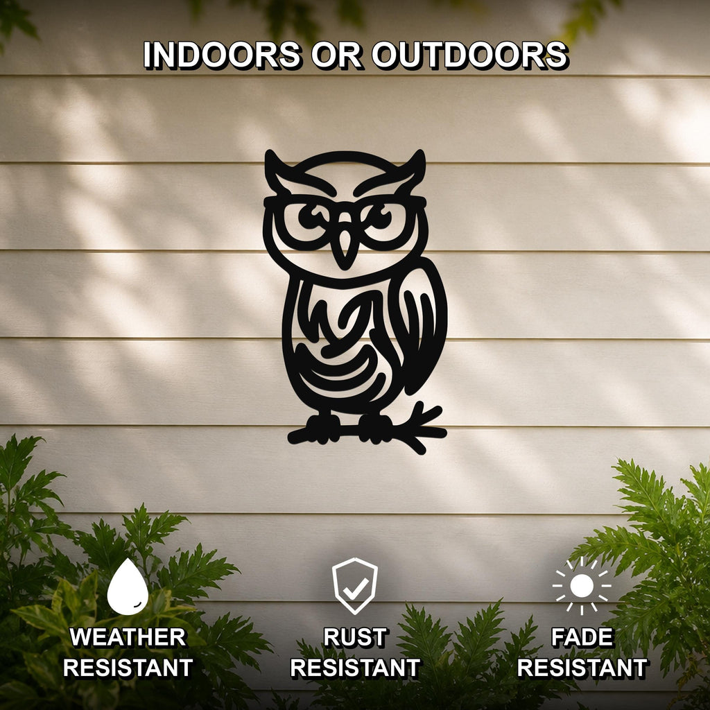 Black metal owl wall art with glasses and internal swirl cutouts, mounted on a light-colored outdoor wall with greenery below.