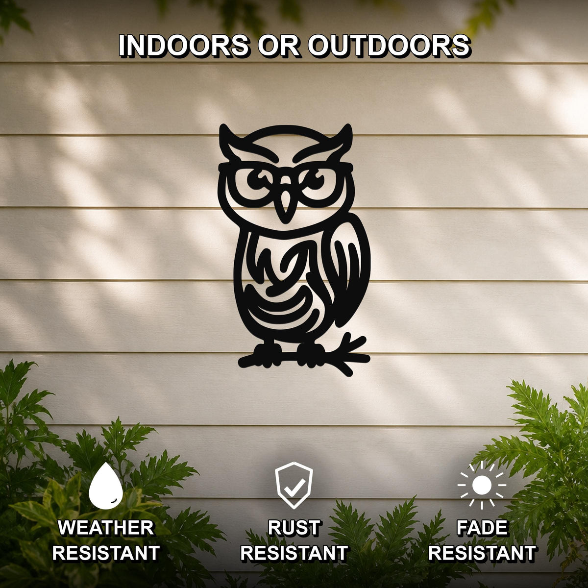 Black metal owl wall art with glasses and internal swirl cutouts, mounted on a light-colored outdoor wall with greenery below.