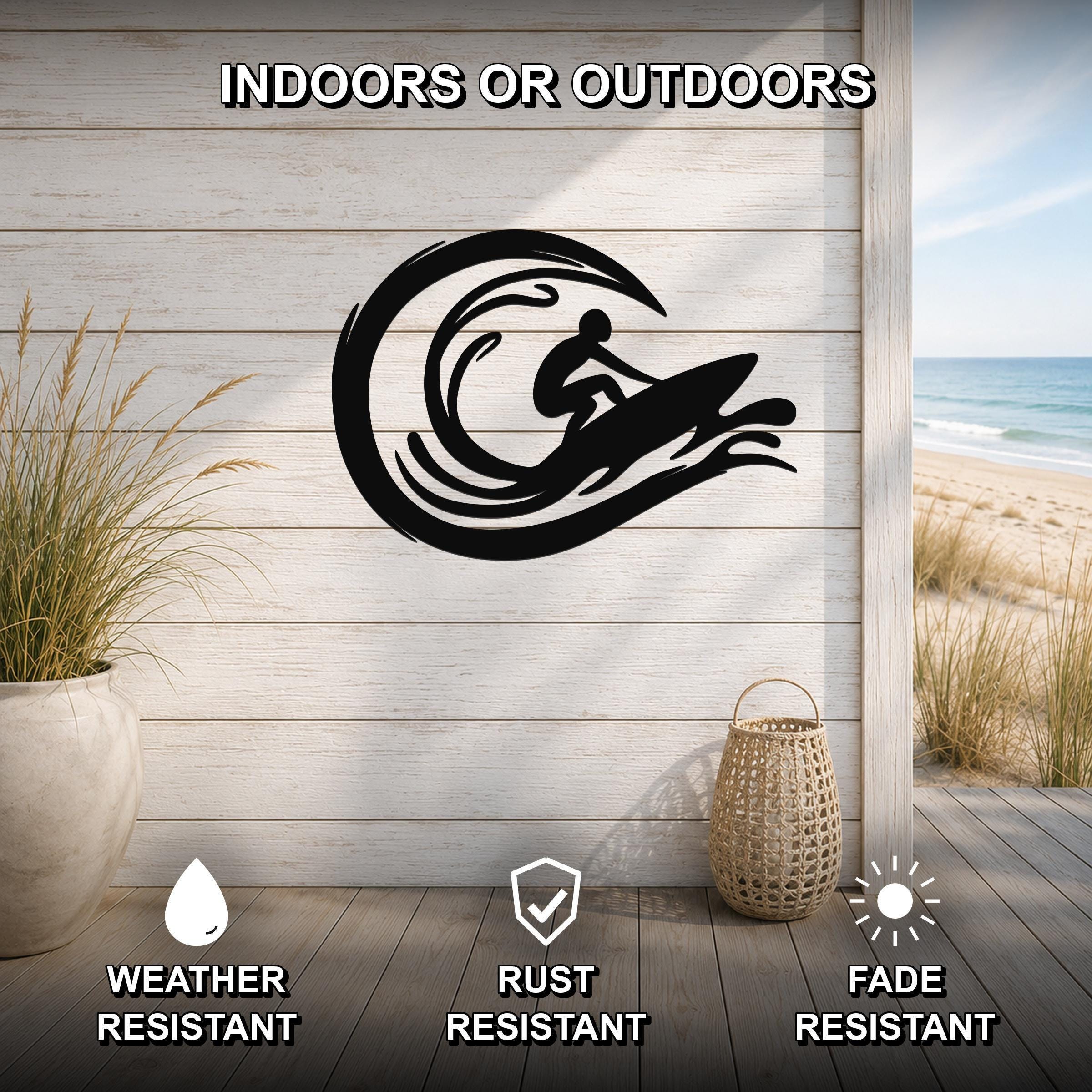 Black metal wall art featuring a surfer silhouette riding a wave, mounted on a light wood wall above a deck with a beach view, weather, rust, and fade resistant.