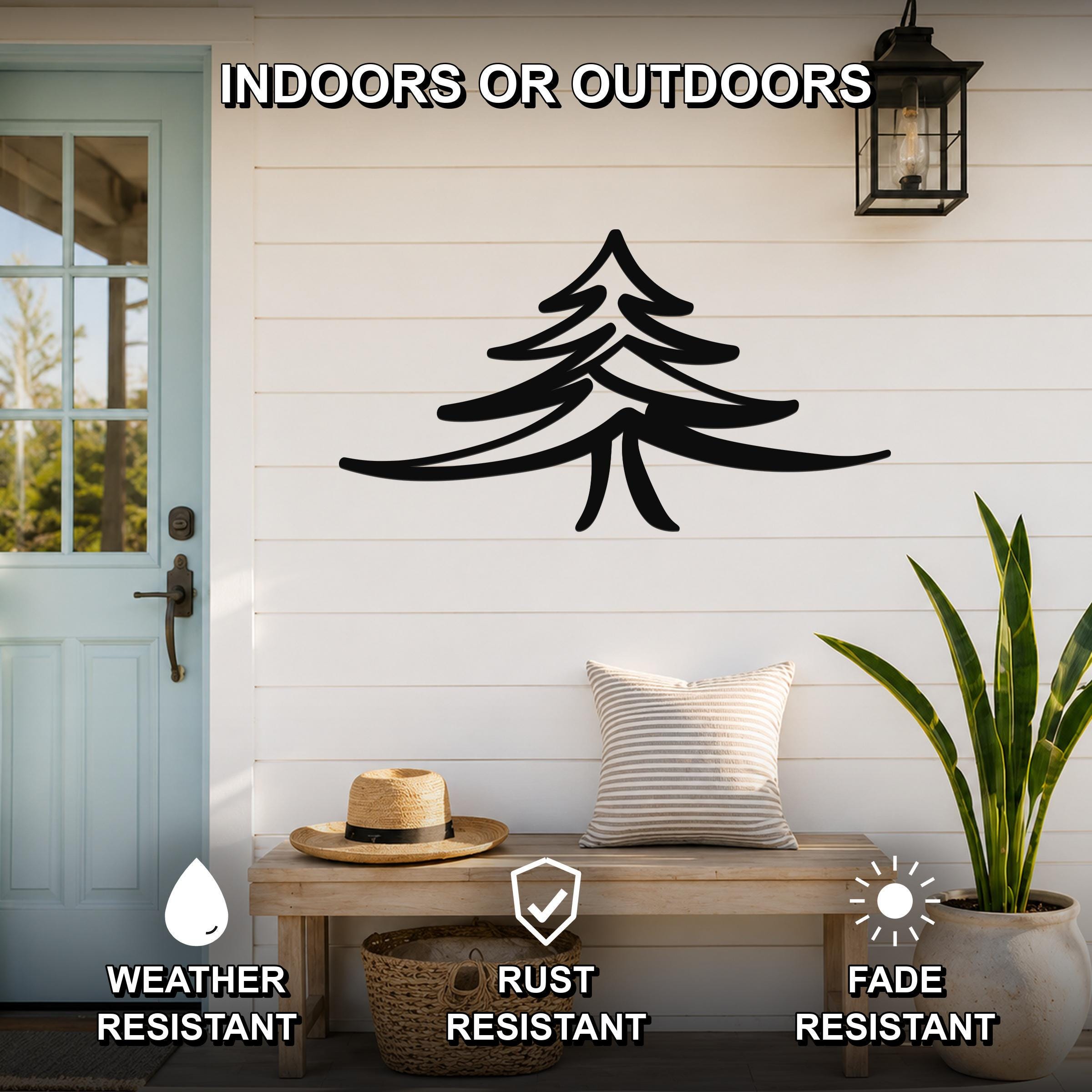 Black metal pine tree wall art with layered branch cutouts, mounted on a white shiplap wall above a wooden bench on a porch.
