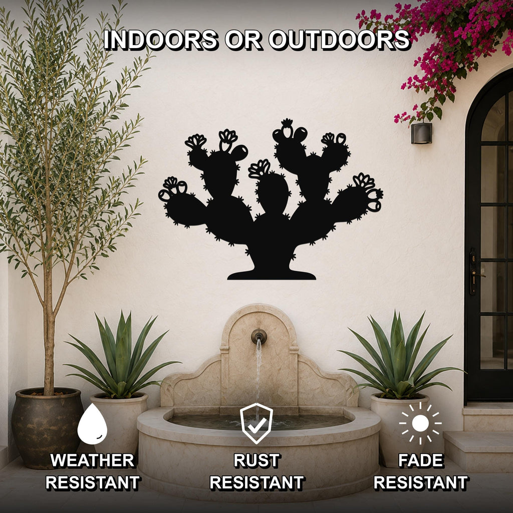Black metal prickly pear cactus wall art with flower and spine cutouts, mounted on an outdoor wall above a stone fountain in a patio setting.
