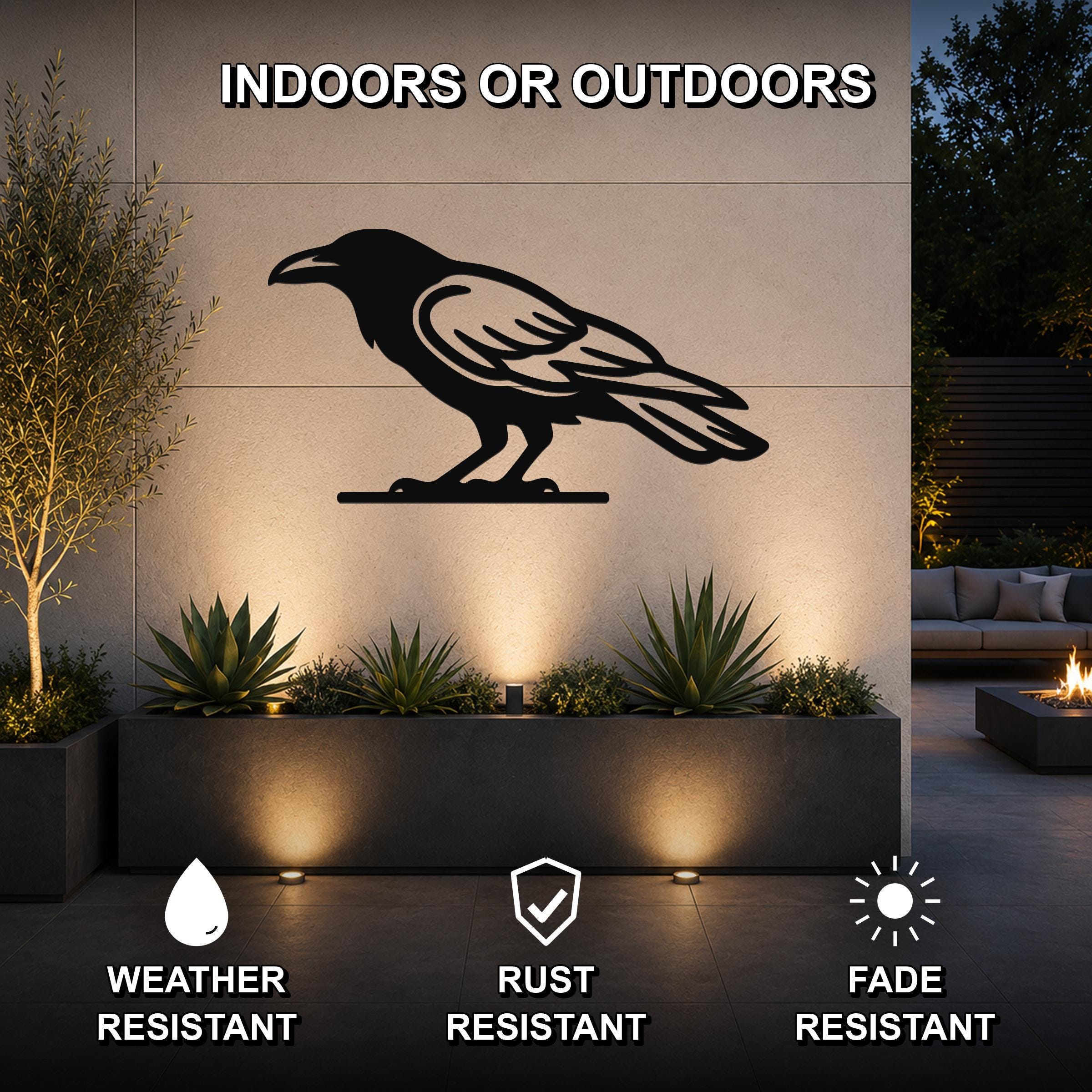 Black metal raven wall art silhouette mounted on an outdoor wall above a planter, with text indicating it is weather, rust, and fade resistant for indoor or outdoor use.