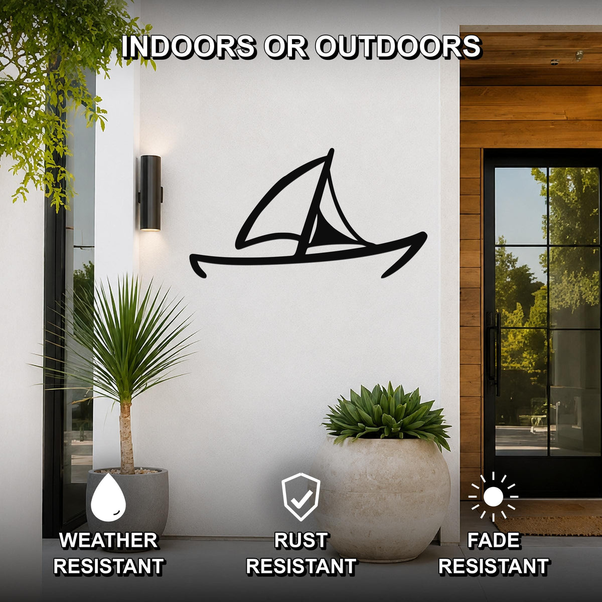 Black metal sailboat wall art with a silhouette design, mounted on a white exterior wall beside a glass door and potted plants, suitable for indoor or outdoor use.