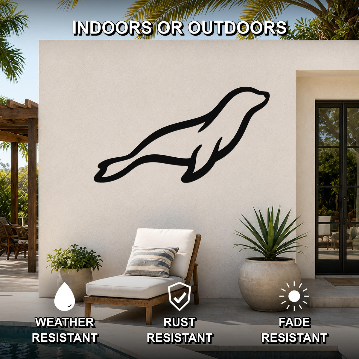 Black metal sea lion wall art silhouette mounted on an outdoor patio wall above a lounge chair, with palm trees and a pool visible in the background.