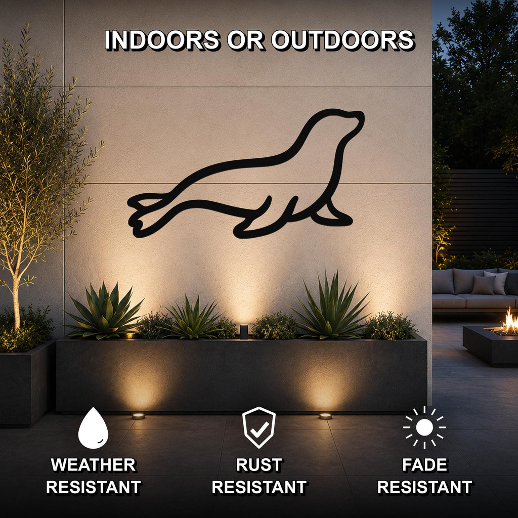 Black metal sea lion wall art silhouette mounted on an outdoor wall above a planter, illuminated by uplights in a modern patio setting.