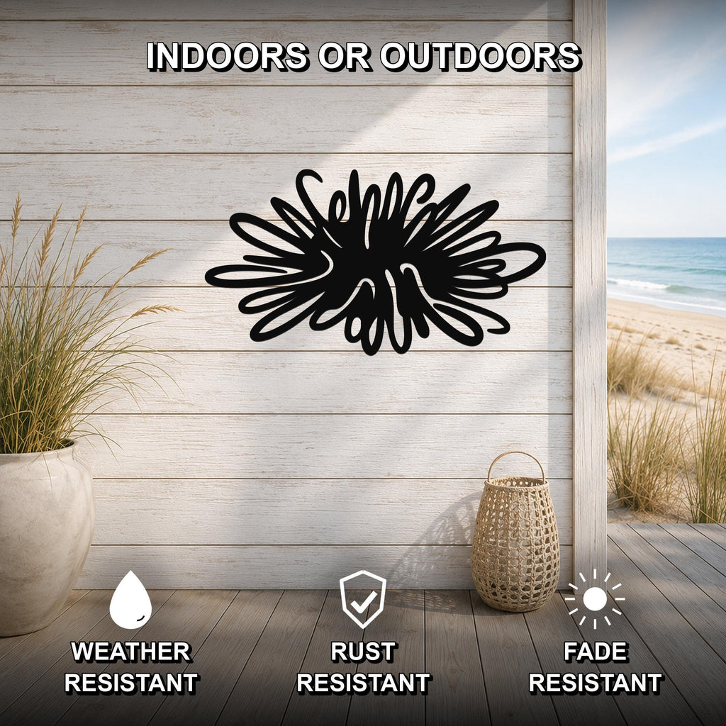 Black metal sea urchin wall art with spiky cutout design, mounted on a light wood plank wall above a deck with a beach view.