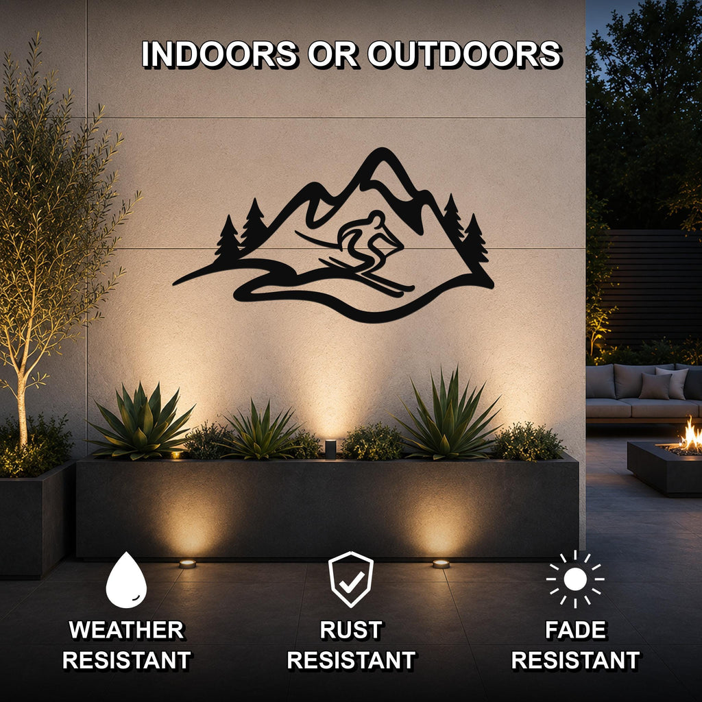 Black metal wall art featuring a skier silhouette within a mountain range and pine trees, mounted on an outdoor wall above a planter with uplighting.