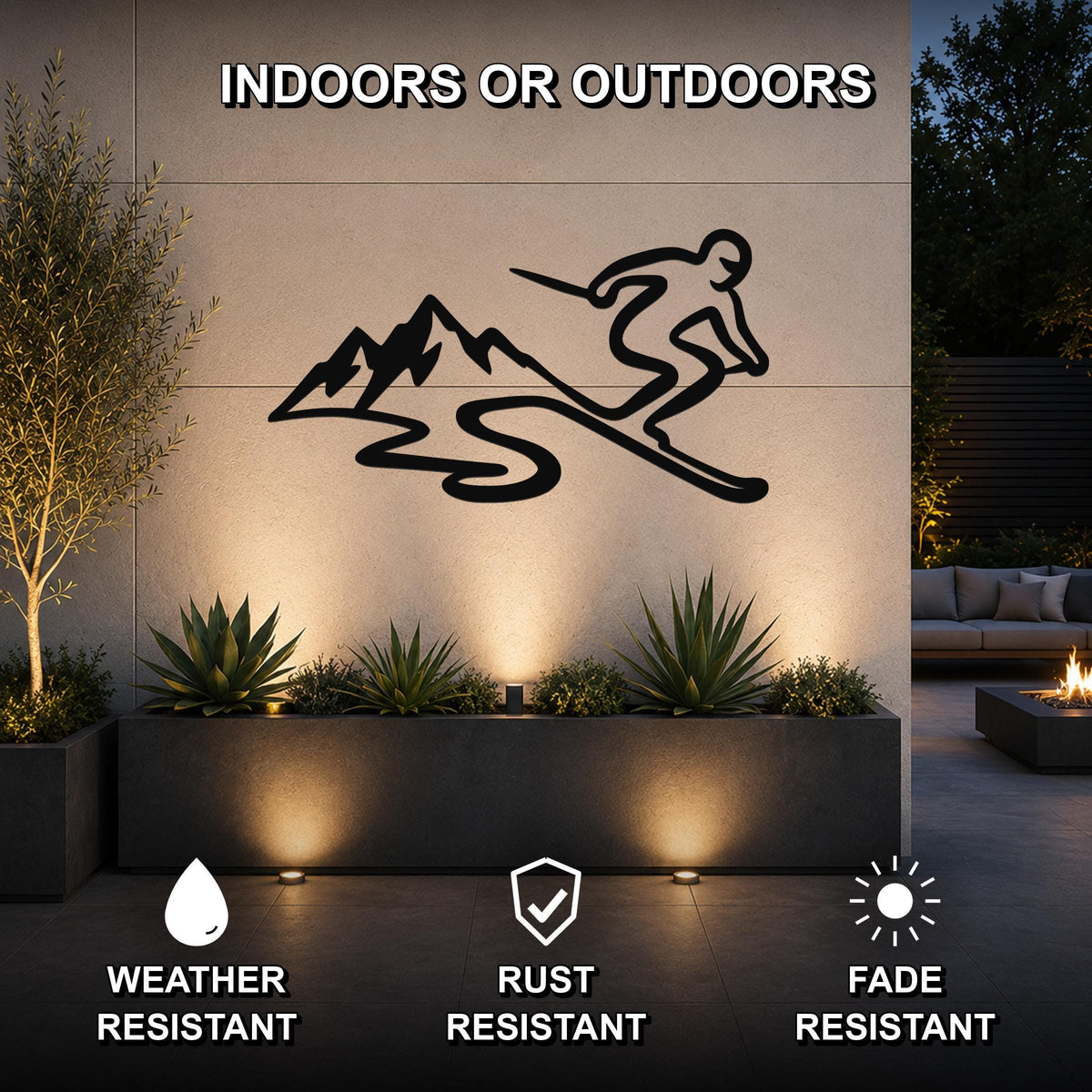 Black metal skier and mountain wall art silhouette mounted on an outdoor patio wall above a planter, with lighting highlighting the scene.