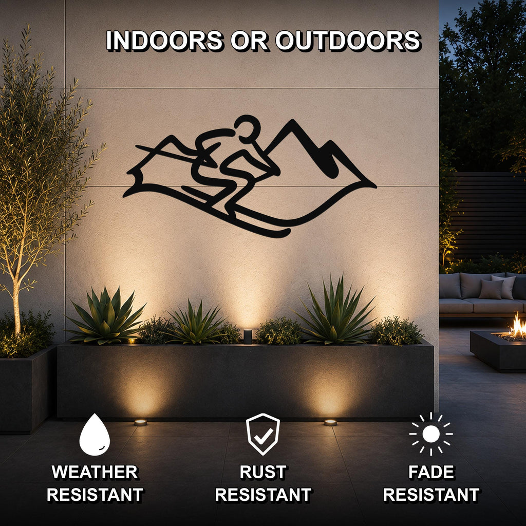 Black metal skier and mountain wall art silhouette mounted on an outdoor patio wall above a planter, with text indicating it is weather, rust, and fade resistant.