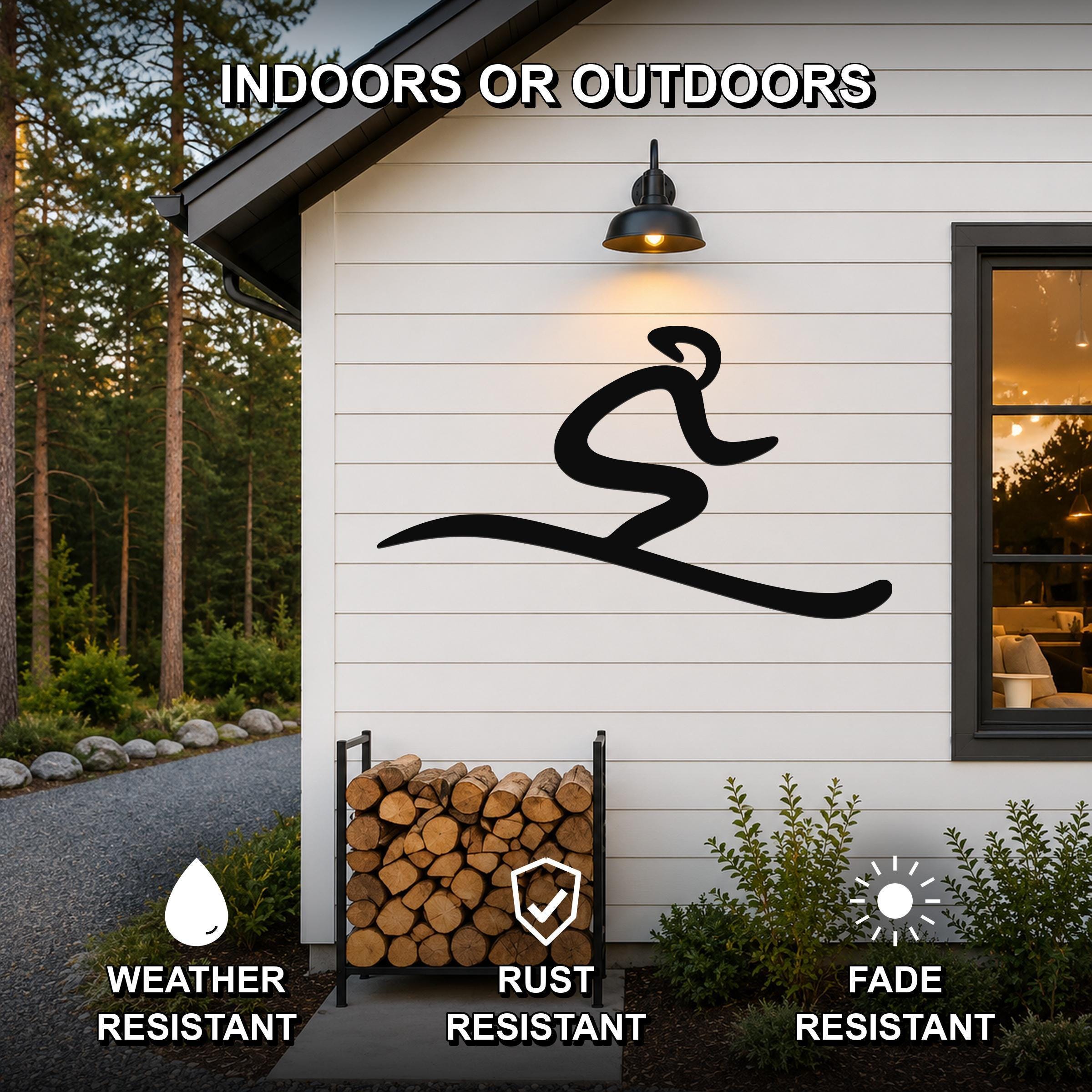 Black metal skiing wall art with a dynamic silhouette, mounted on a white exterior wall above a firewood rack, weather and fade resistant.