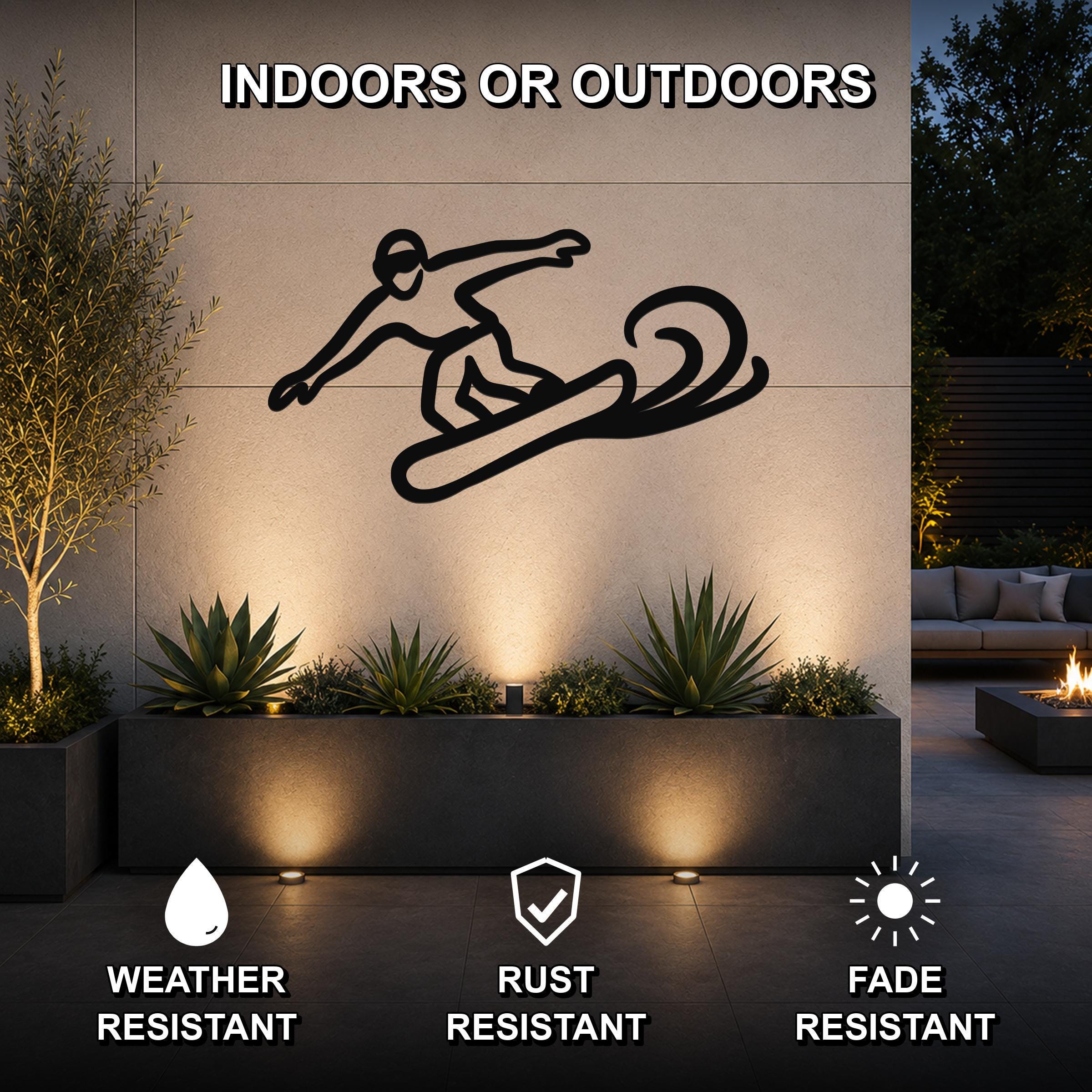 Black metal snowboarder silhouette wall art with motion lines, mounted on an outdoor wall above a planter in a patio setting.