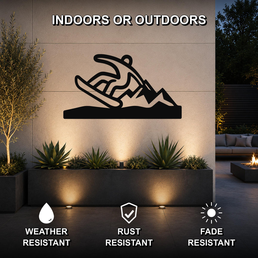Black metal snowboarder wall sculpture with mountain silhouette, mounted on an outdoor patio wall above a planter with uplighting.