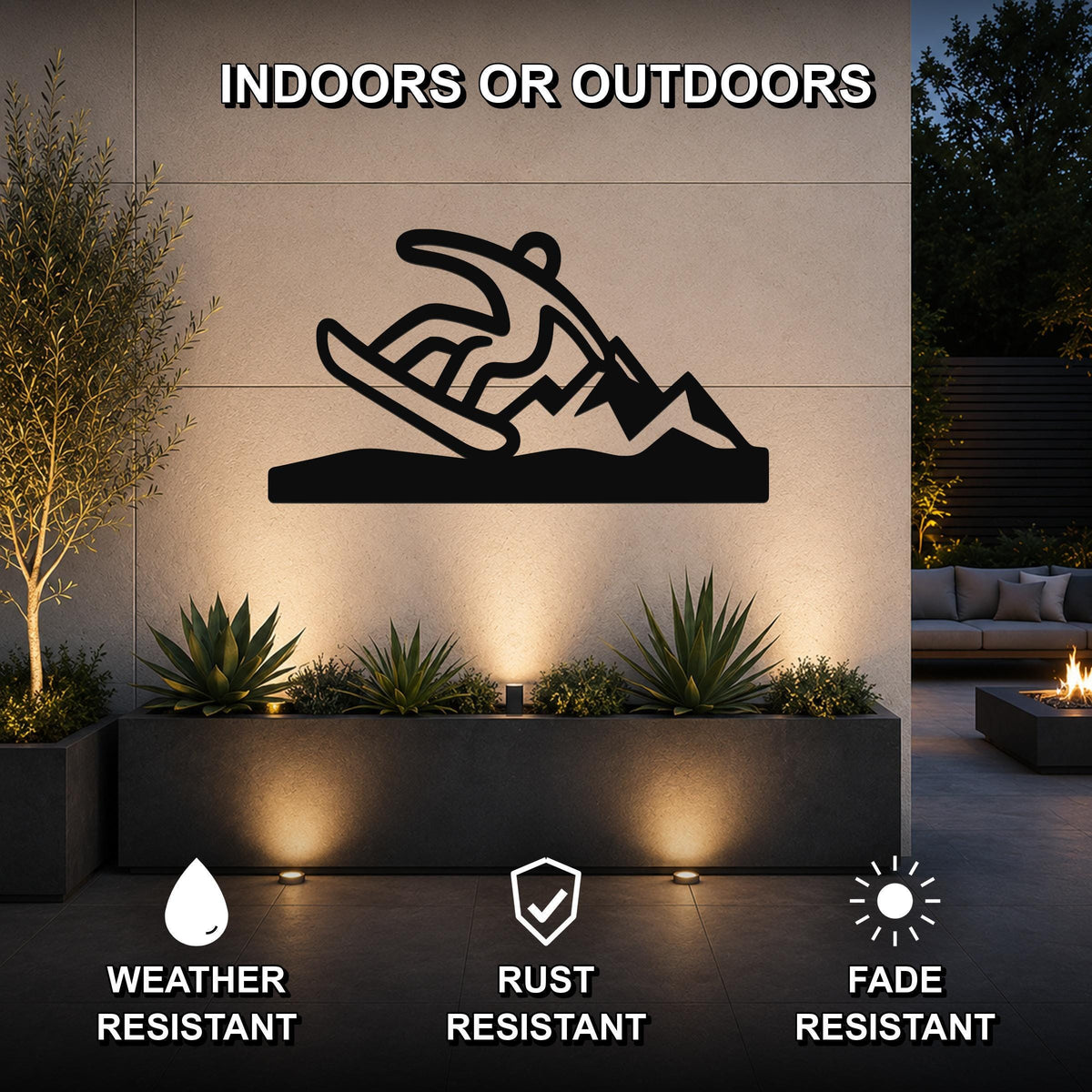 Black metal snowboarder wall sculpture with mountain silhouette, mounted on an outdoor patio wall above a planter with uplighting.