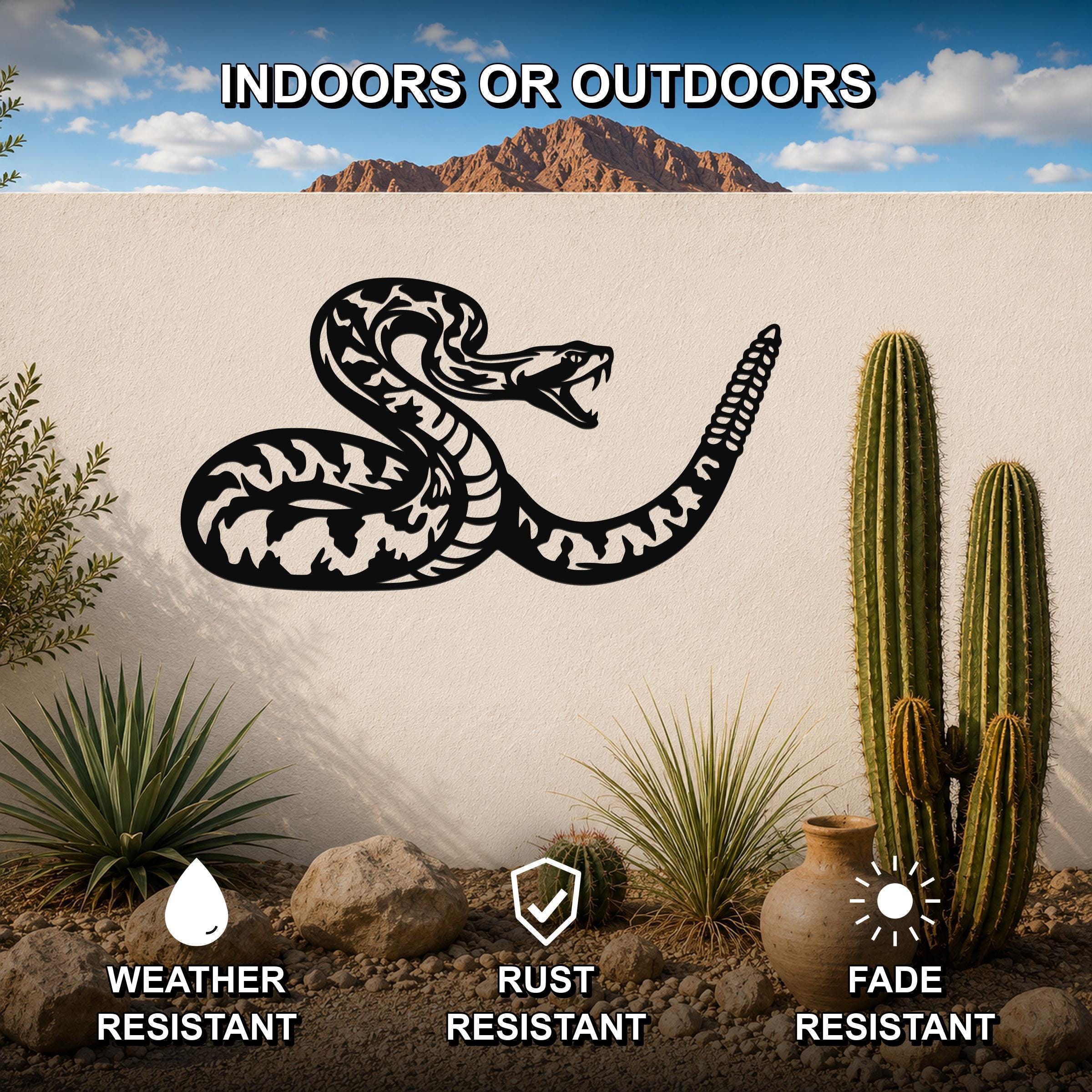Black metal rattlesnake wall art with detailed internal cutouts, mounted on an outdoor wall in a desert garden setting with cacti and rocks.