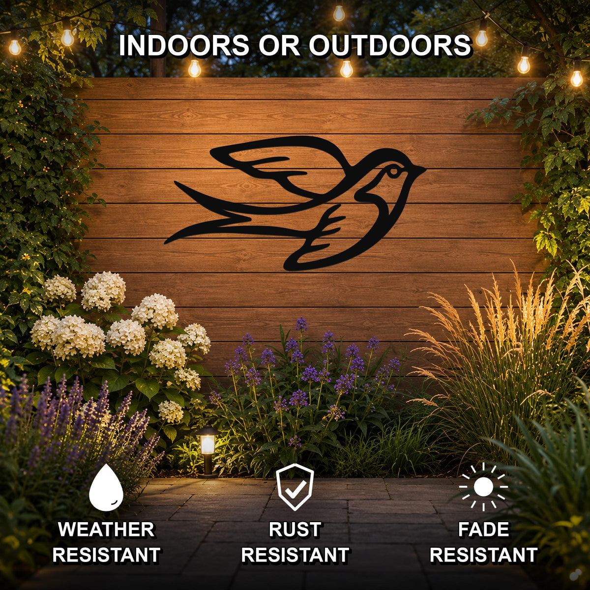 Black metal swallow bird wall art silhouette mounted on a wooden outdoor wall, displayed above a garden with flowers and string lights, weather, rust, and fade resistant.