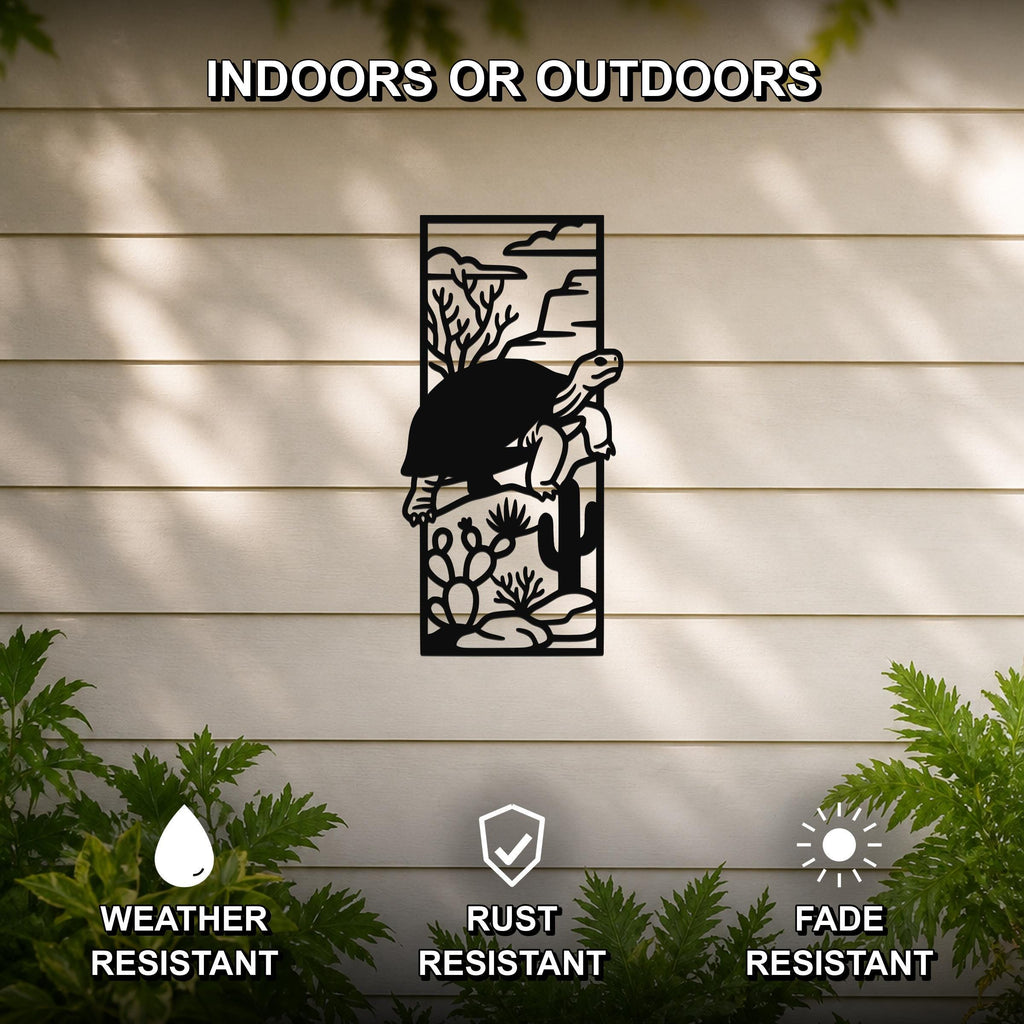 Black metal wall art featuring a tortoise silhouette climbing over cacti and desert plants, mounted on a light-colored outdoor wall with greenery below.