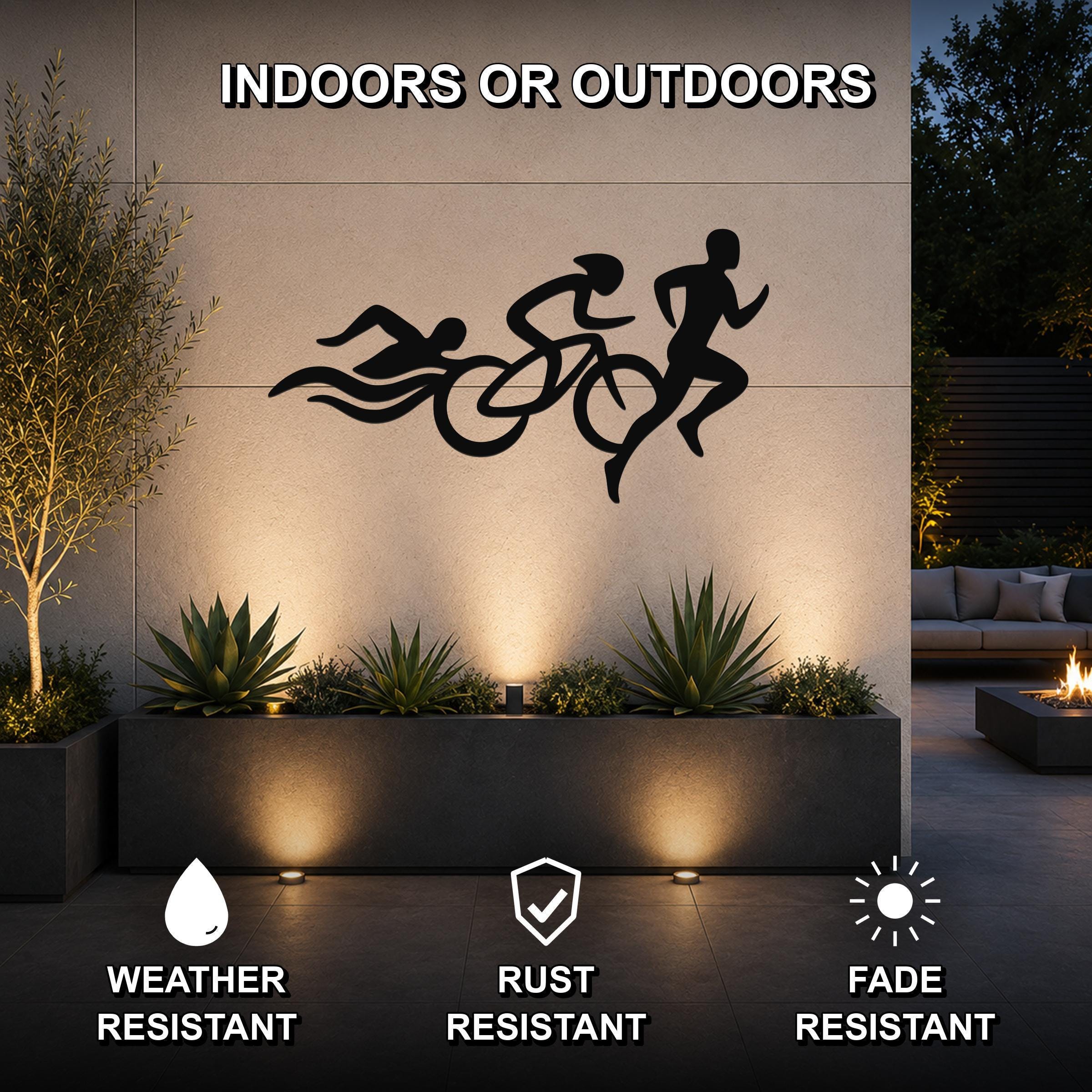Black metal triathlon wall art with swim, bike, and run silhouettes, mounted on an outdoor wall above a planter in a modern patio setting.