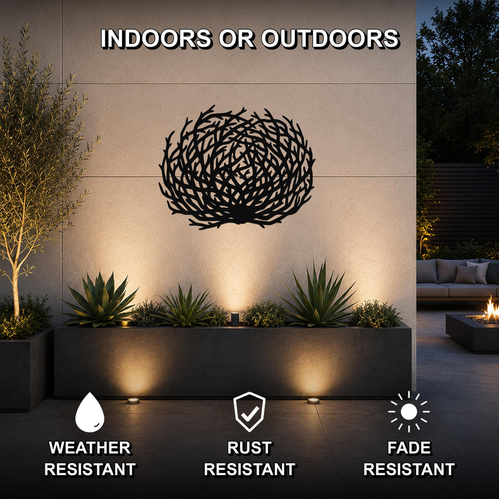 Black metal tumbleweed wall art with intricate branch cutouts, mounted on an outdoor wall above a planter in a modern patio setting.