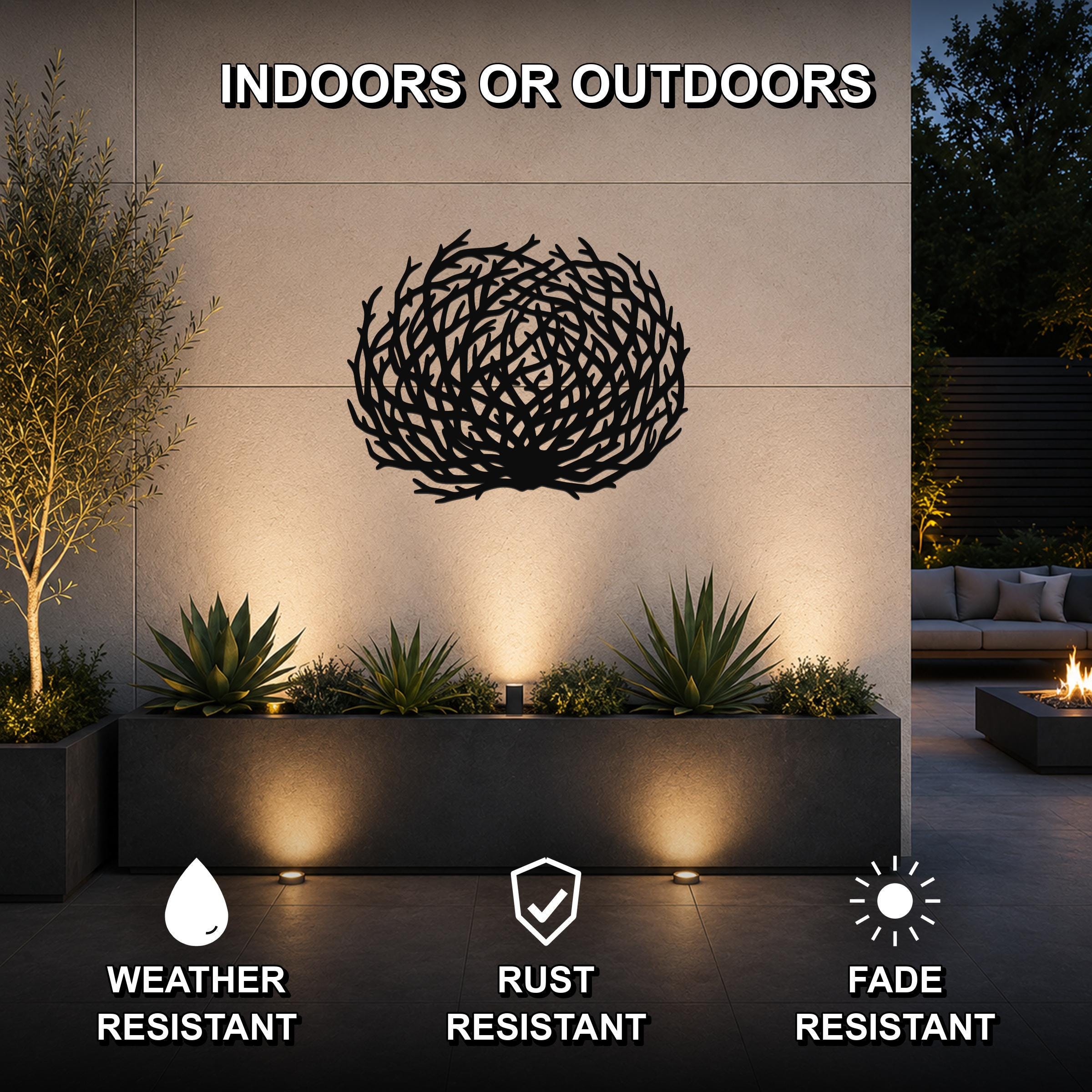 Black metal tumbleweed wall art with intricate branch cutouts, mounted on an outdoor wall above a planter in a modern patio setting.