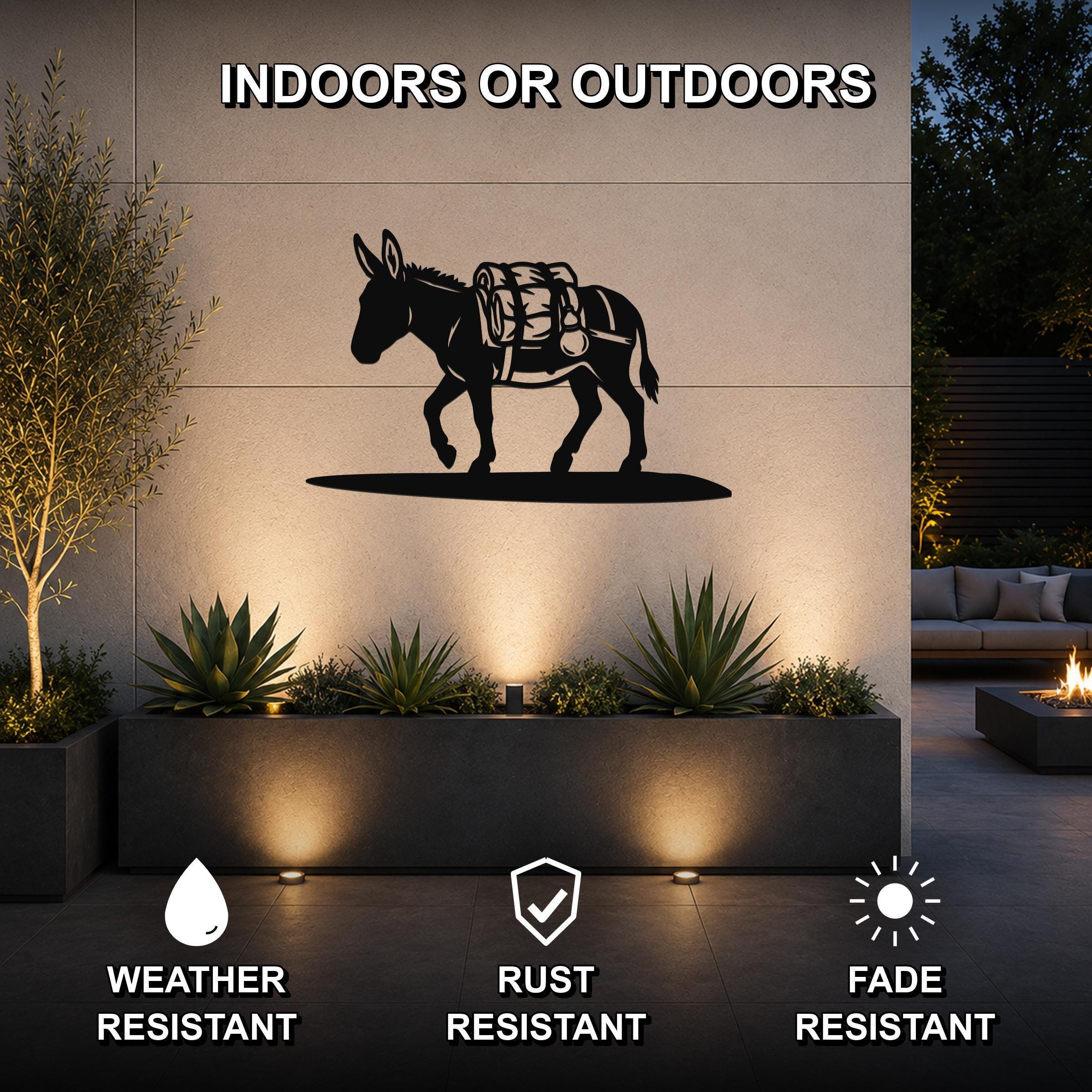 Black metal burro wall art with a backpack silhouette, mounted on an outdoor wall above a planter in a modern patio setting.