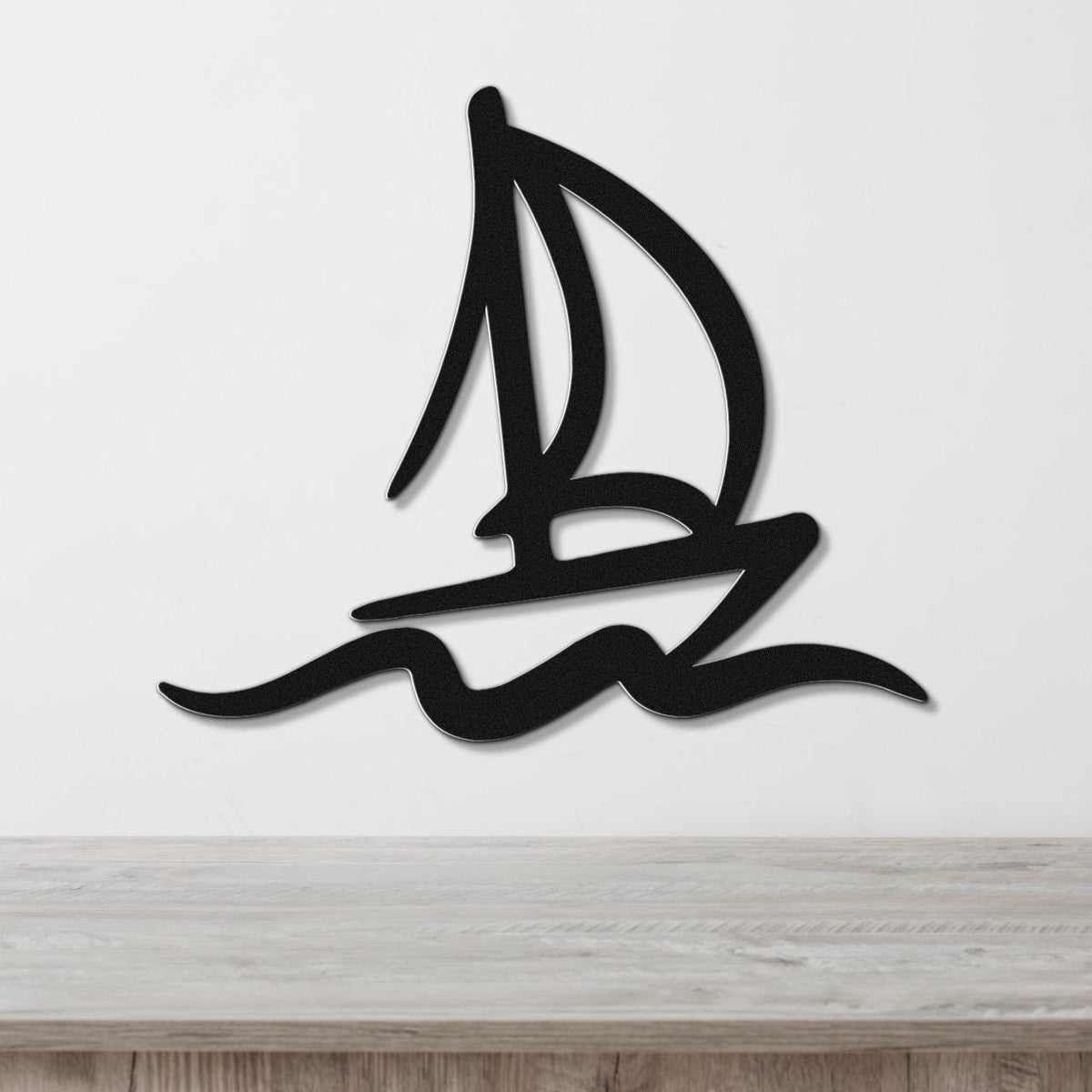 Black metal sailboat wall art with wave cutouts, mounted on a white wall above a wooden surface.