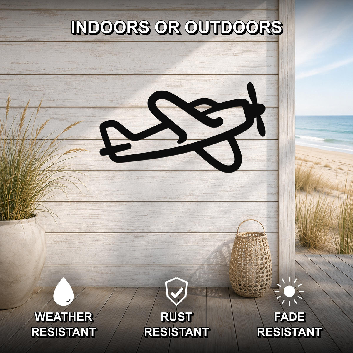 Black metal airplane wall art silhouette mounted on a light wood plank wall above a wooden deck, with a beach view visible through an opening.