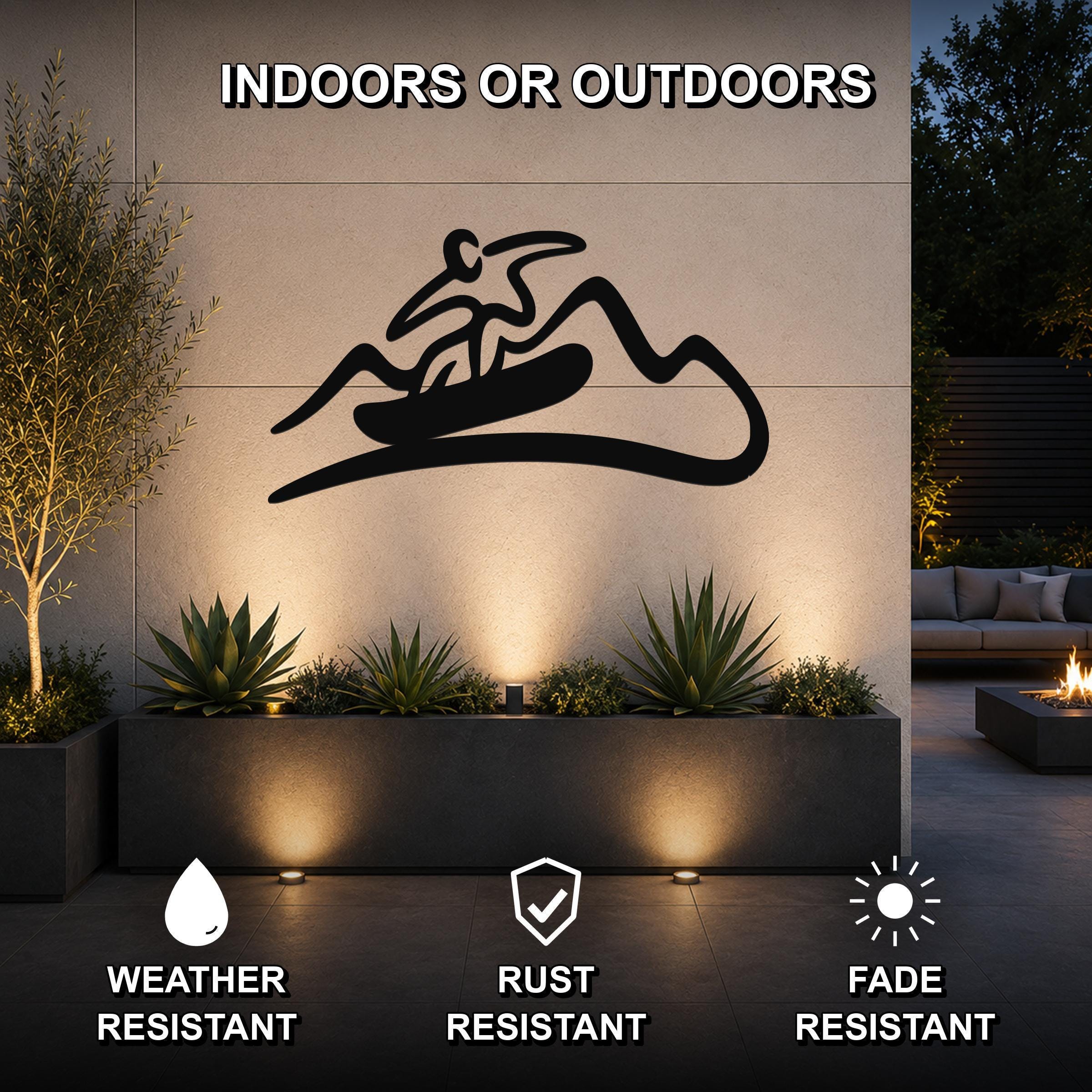 Black metal wall art silhouette of a snowboarder on a mountain, mounted on an outdoor wall above a planter with succulents, in a modern patio setting.