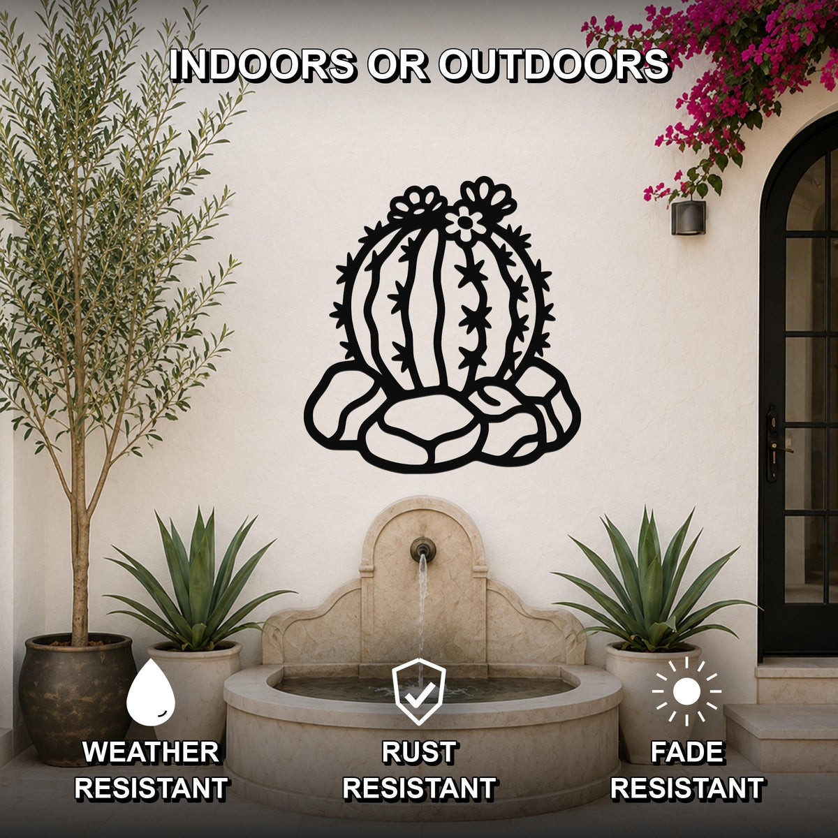 Black metal barrel cactus wall art with flower and spine cutouts, mounted on a white outdoor wall above a stone fountain.