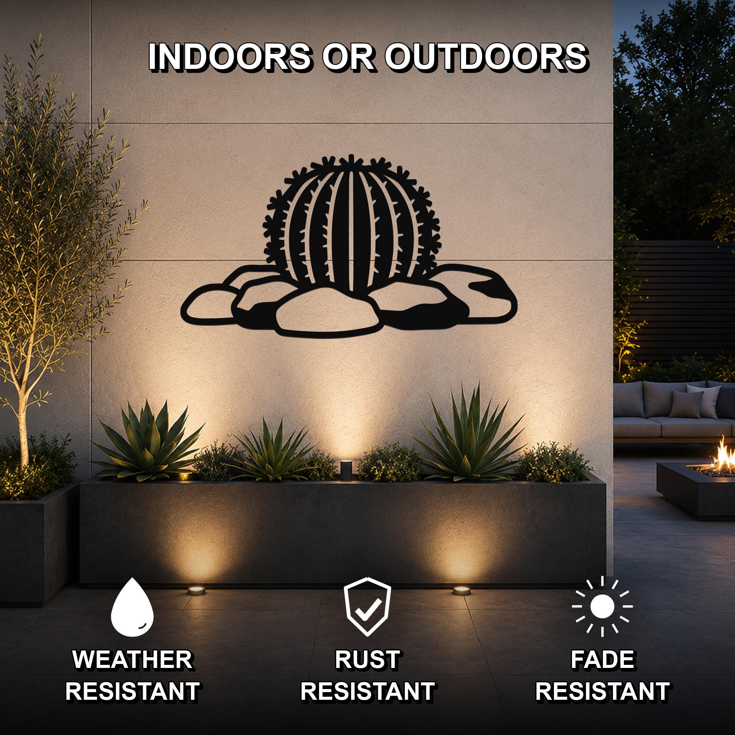 Black metal barrel cactus wall art with spines and rocks cutout, mounted on an outdoor wall above a planter in a patio setting.