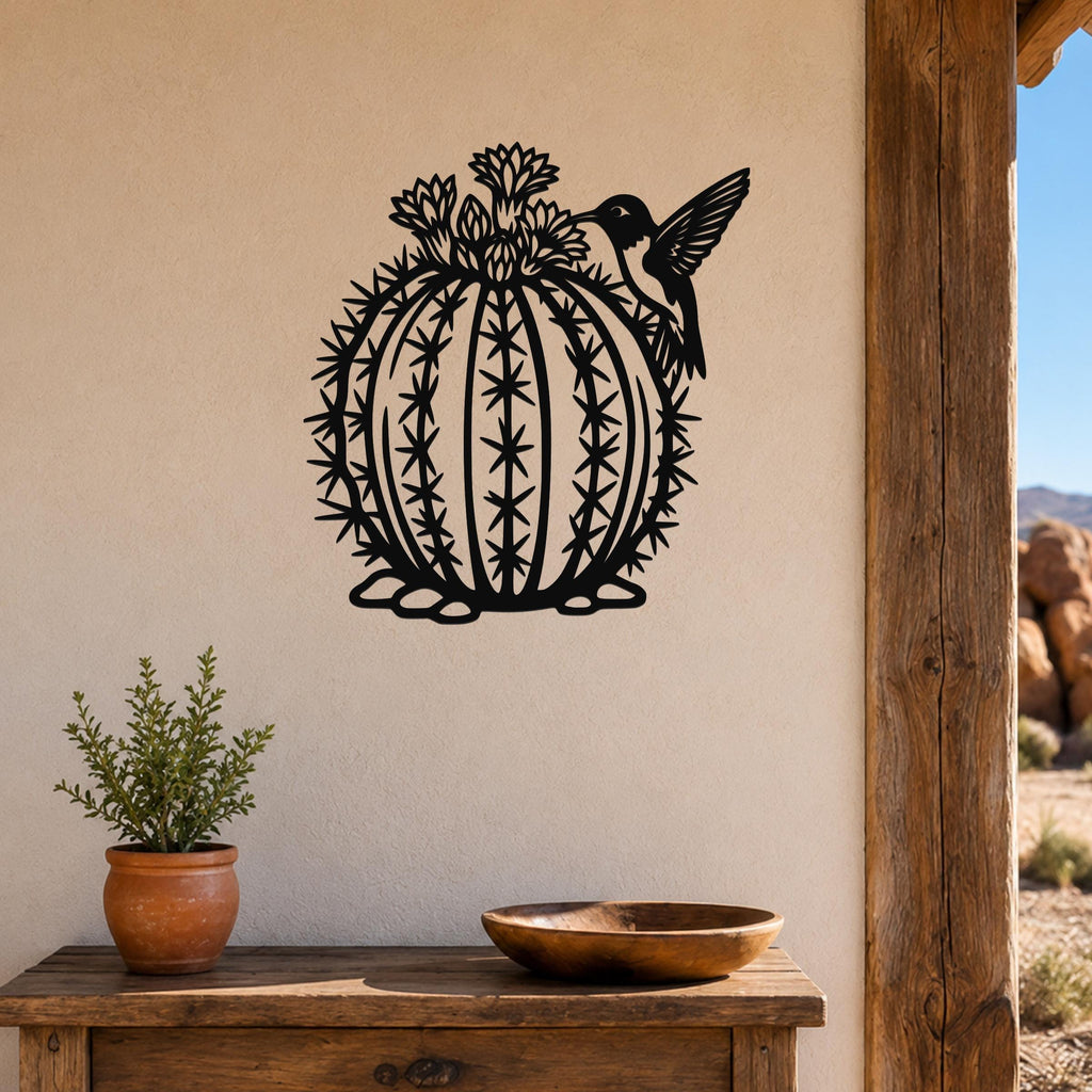 Black metal barrel cactus wall sculpture with flower and hummingbird cutouts, mounted on a beige wall above a wooden table.