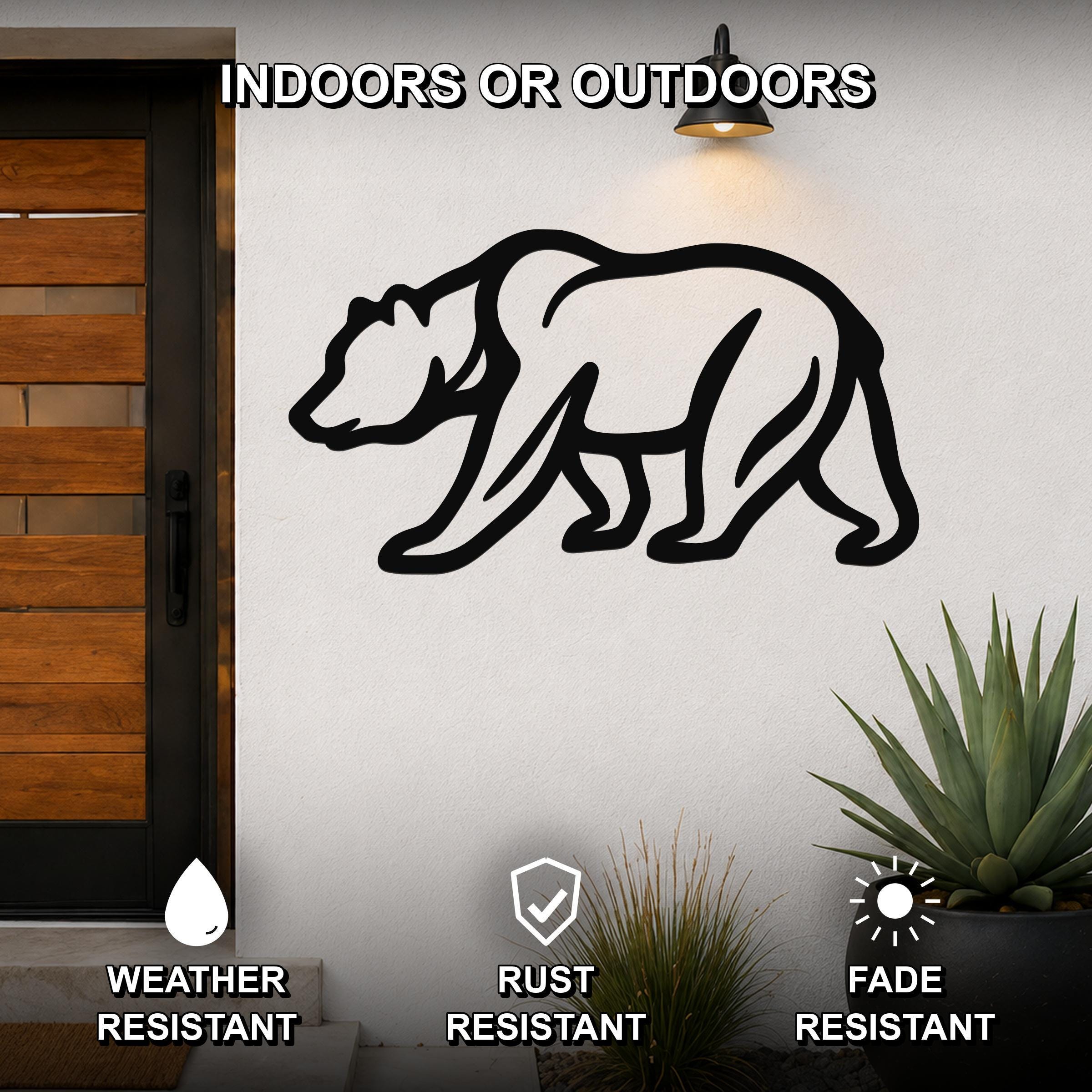Black metal bear silhouette wall art mounted on a white exterior wall beside a wooden door, with a potted succulent below and a wall light above.
