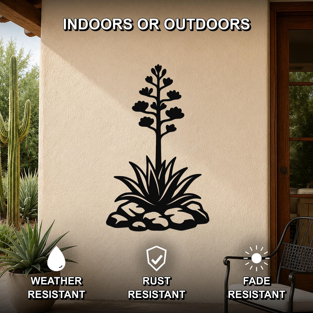 Black metal agave wall sculpture with blooming flower and leaf cutouts, mounted on a beige outdoor wall with cactus and patio furniture in the background.