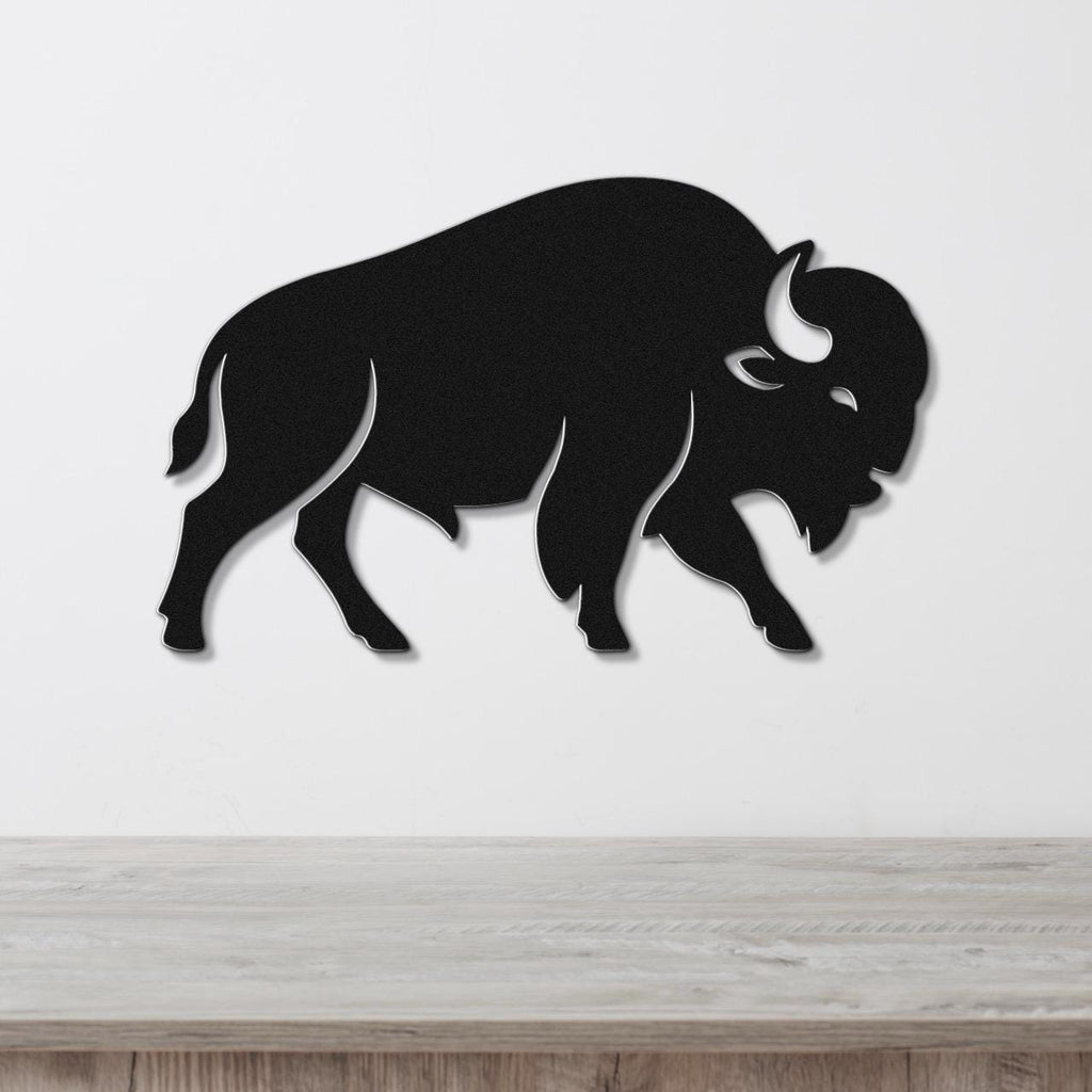 Black metal buffalo wall art silhouette with horn and eye cutouts, mounted on a white wall above a light wood counter.
