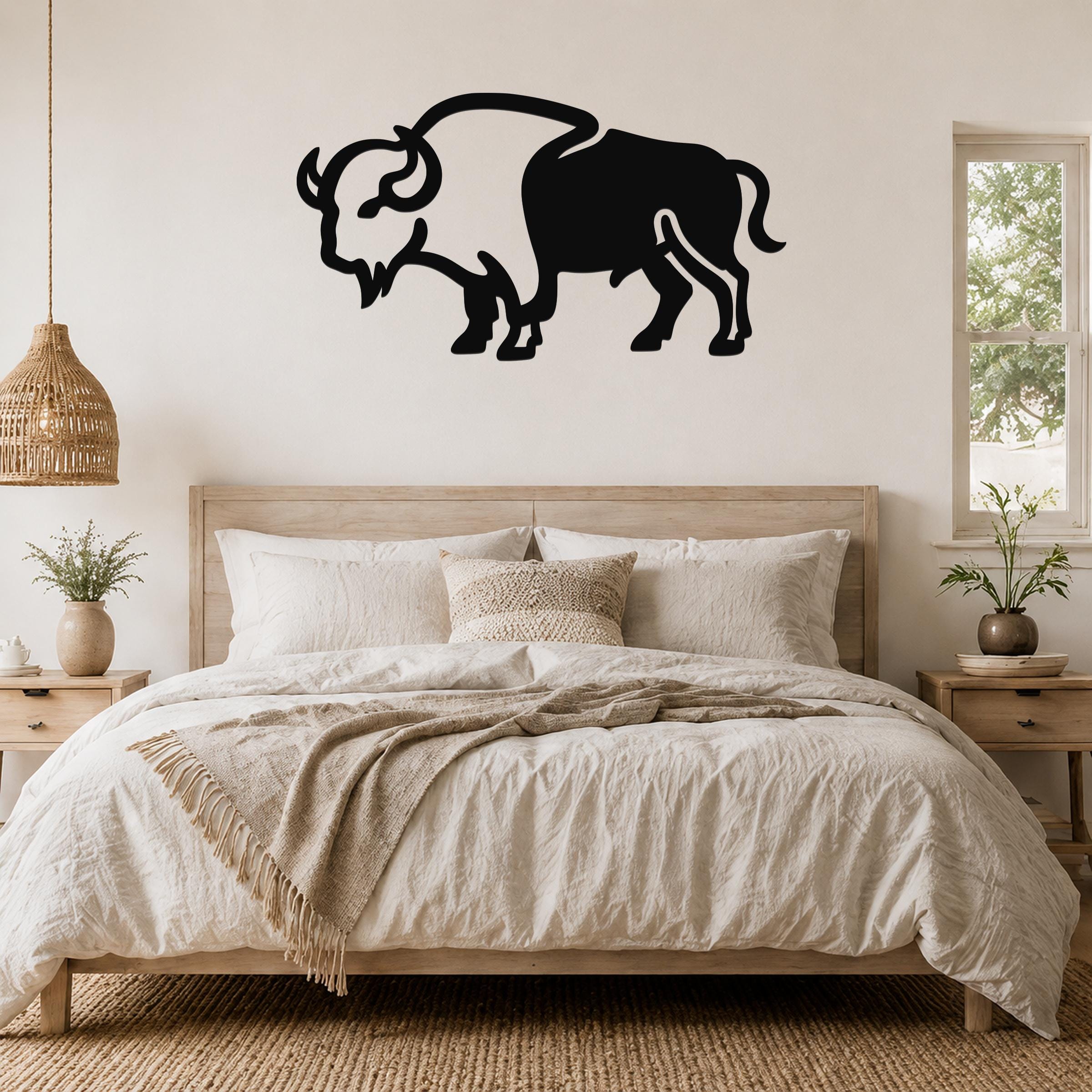 Black metal buffalo silhouette wall art mounted above a wooden bed in a neutral bedroom.
