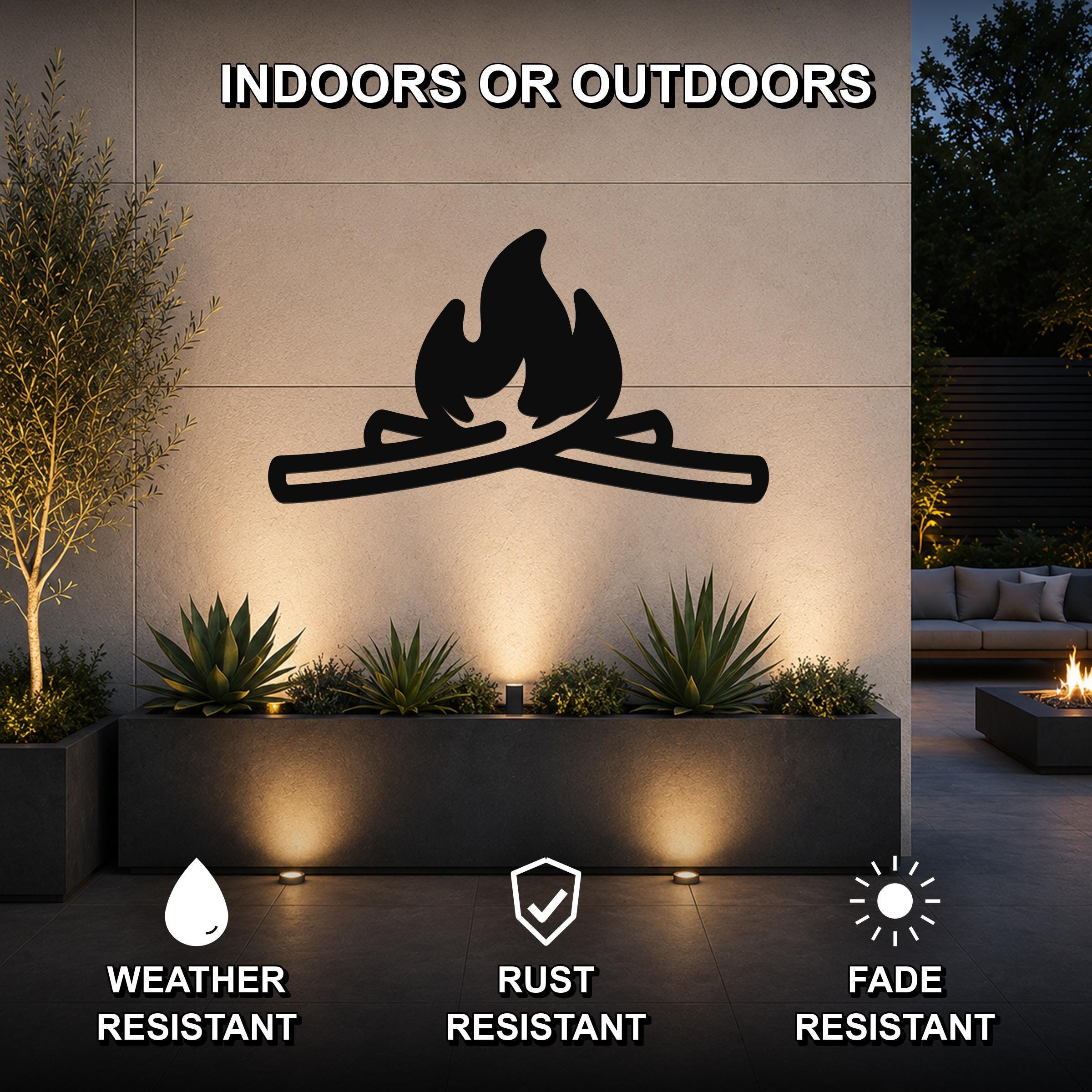 Black metal campfire silhouette wall art with crossed logs and flame cutouts, mounted on an outdoor wall above a planter in a patio setting.