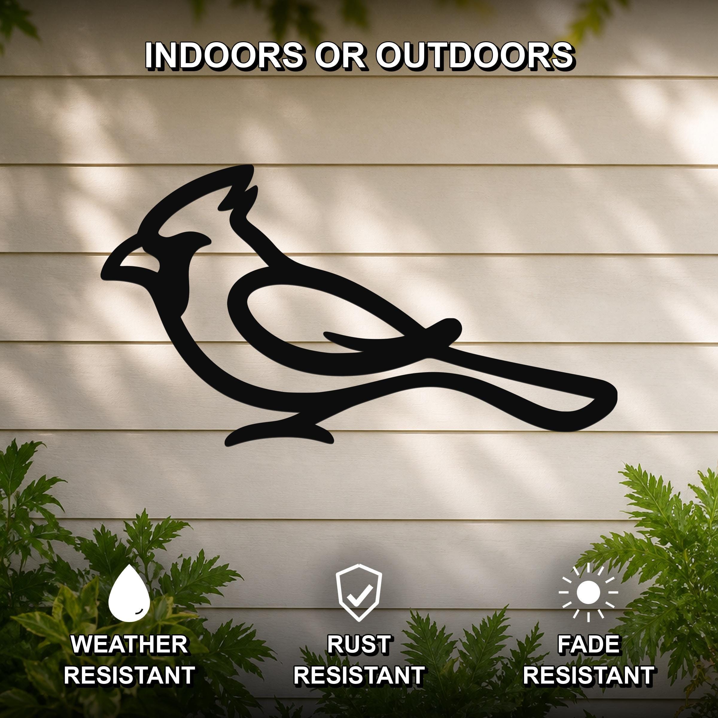 Black metal cardinal wall art in silhouette form, mounted on a light-colored outdoor wall with greenery, weather resistant, rust resistant, and fade resistant.