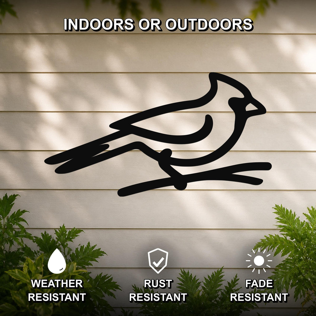 Black metal cardinal wall art silhouette perched on a branch, mounted on a light-colored outdoor wall with greenery, weather resistant, rust resistant, and fade resistant.
