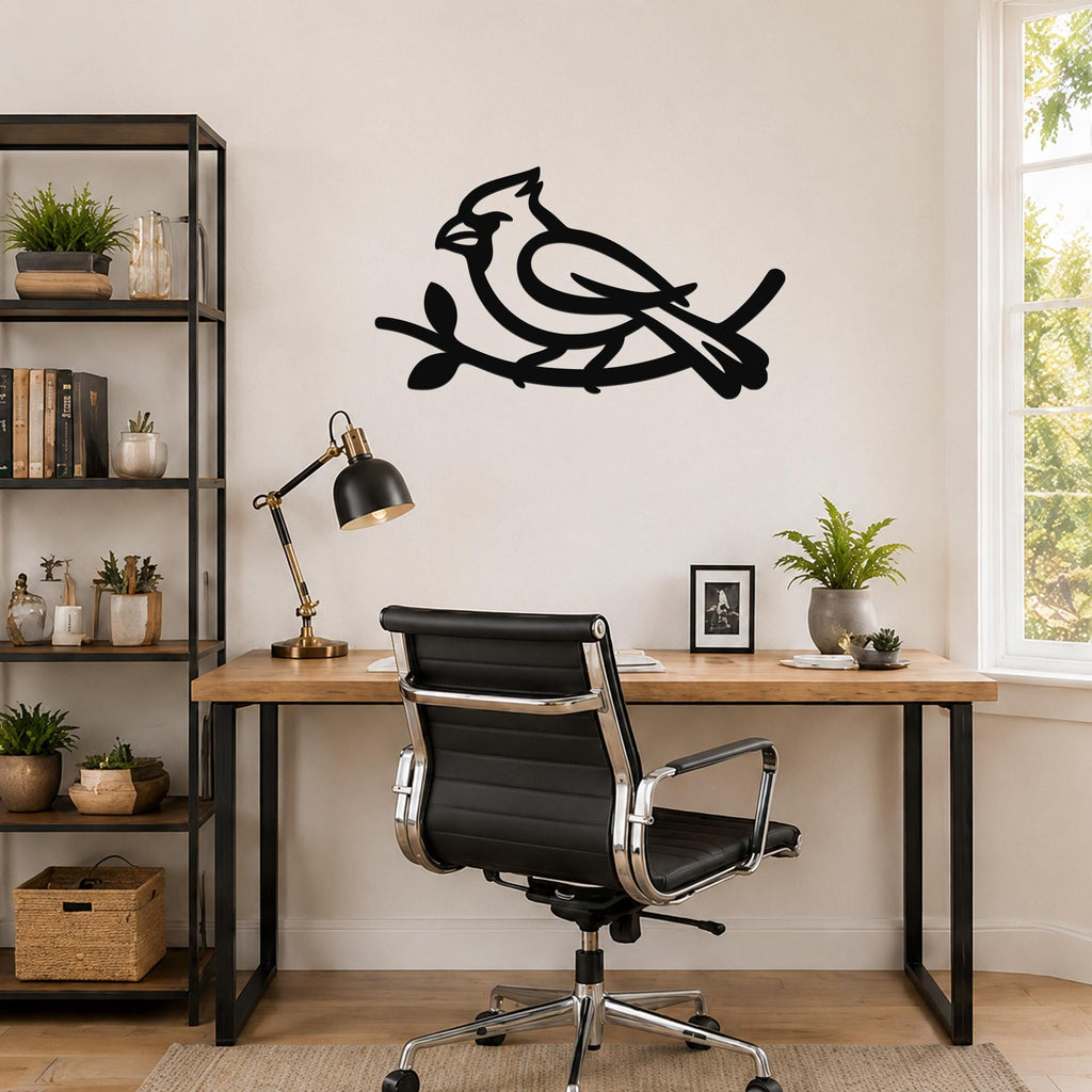 Black metal cardinal wall art in a bold silhouette, perched on a branch, mounted above a wooden desk in a home office.