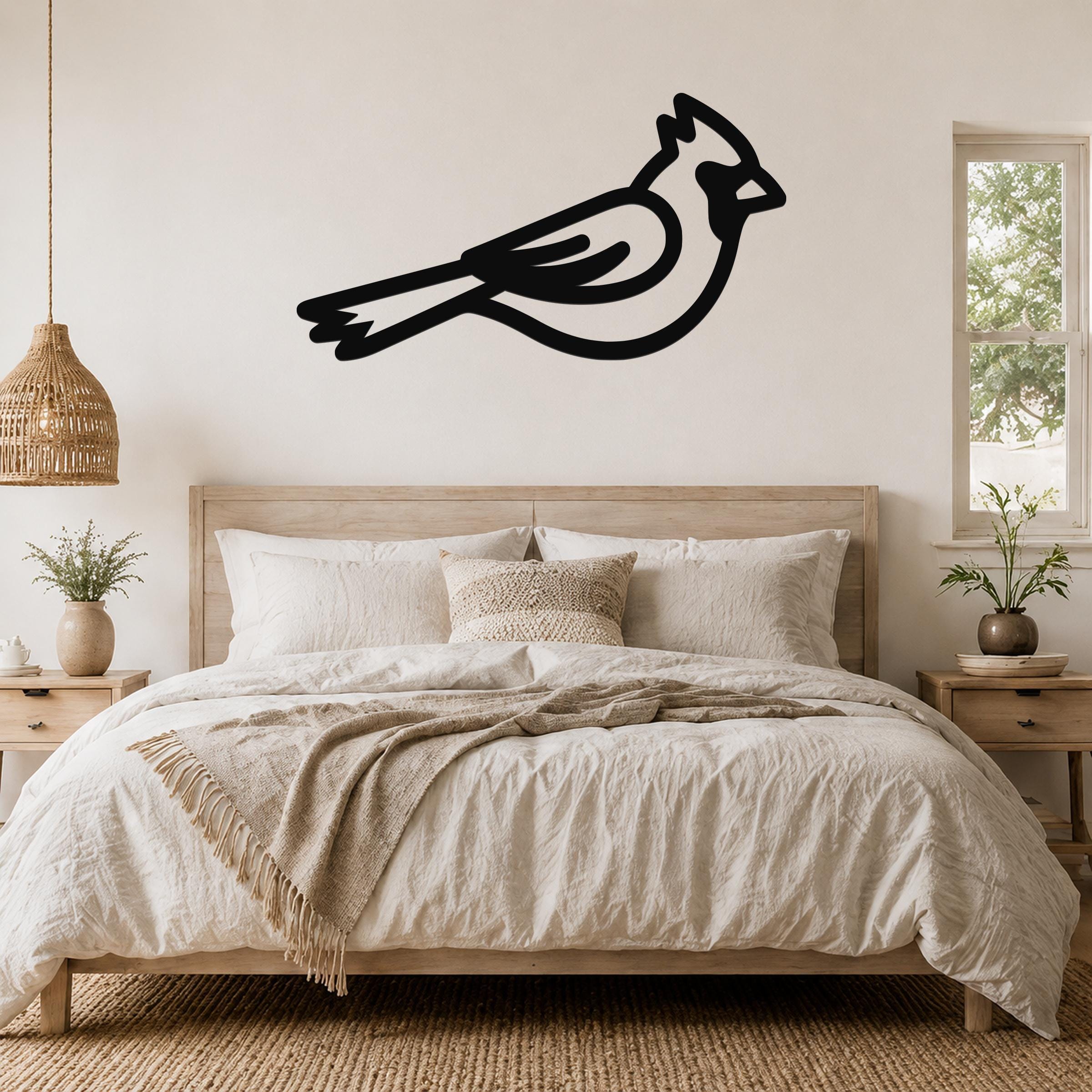 Black metal cardinal wall art silhouette mounted above a bed in a neutral bedroom.