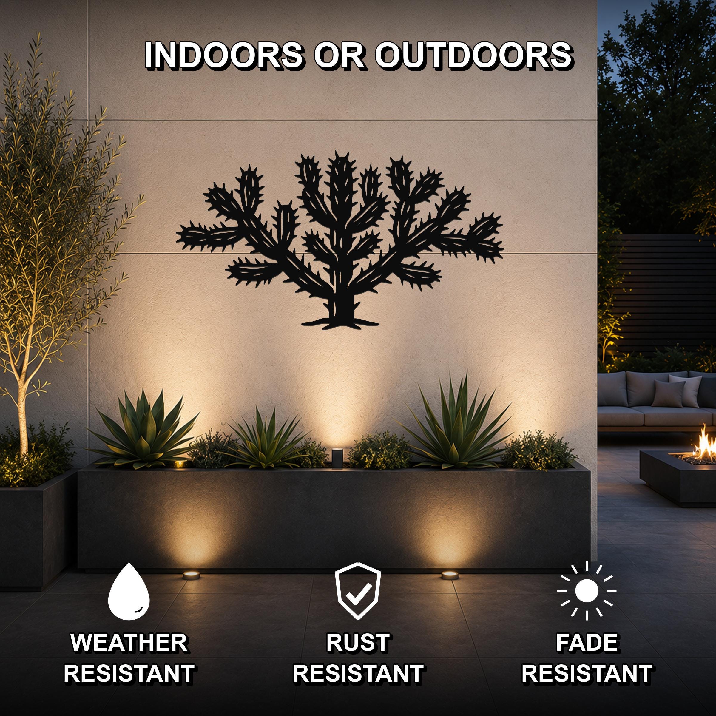 Black metal Cholla cactus wall art with spiky branch cutouts, mounted on an outdoor wall above a planter in a patio setting.