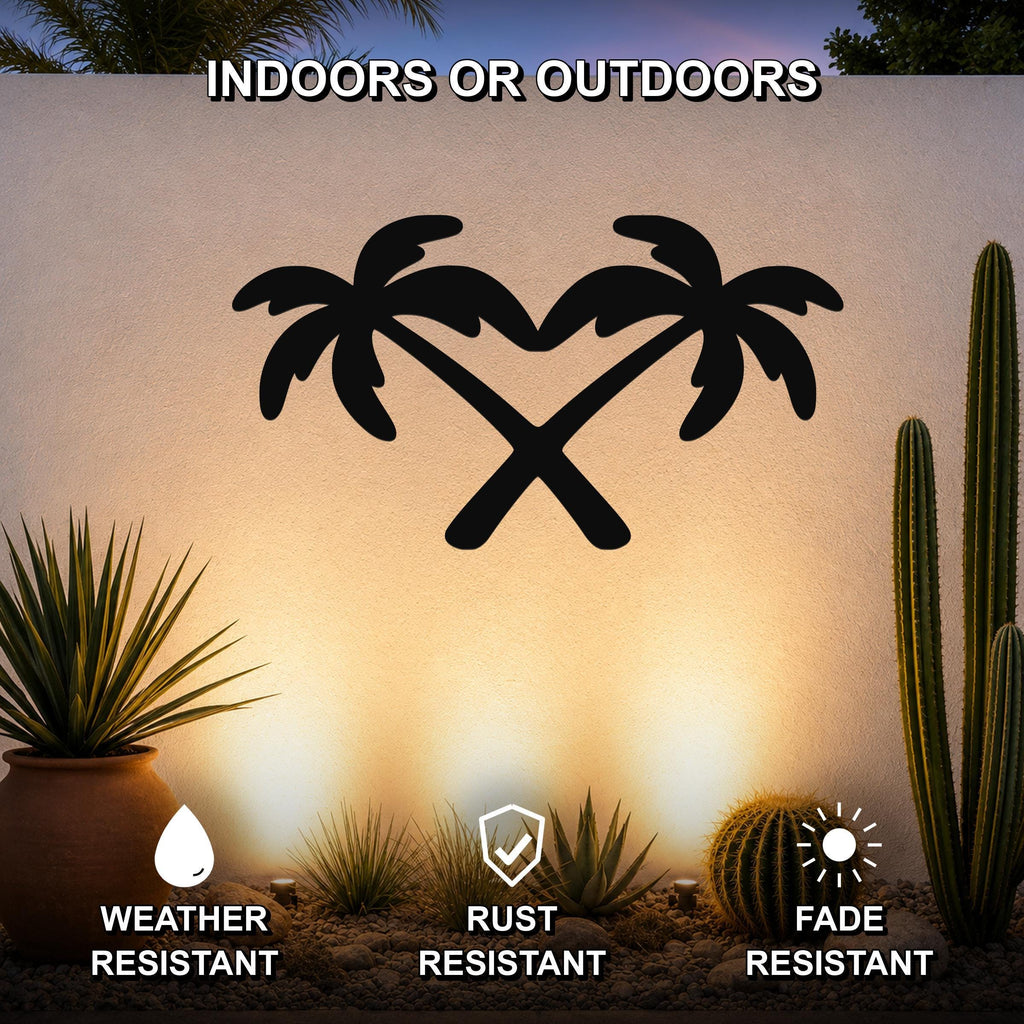 Black metal palm tree wall art with crossed trunks forming a heart shape, mounted on an outdoor wall above a desert garden with cacti and succulents.