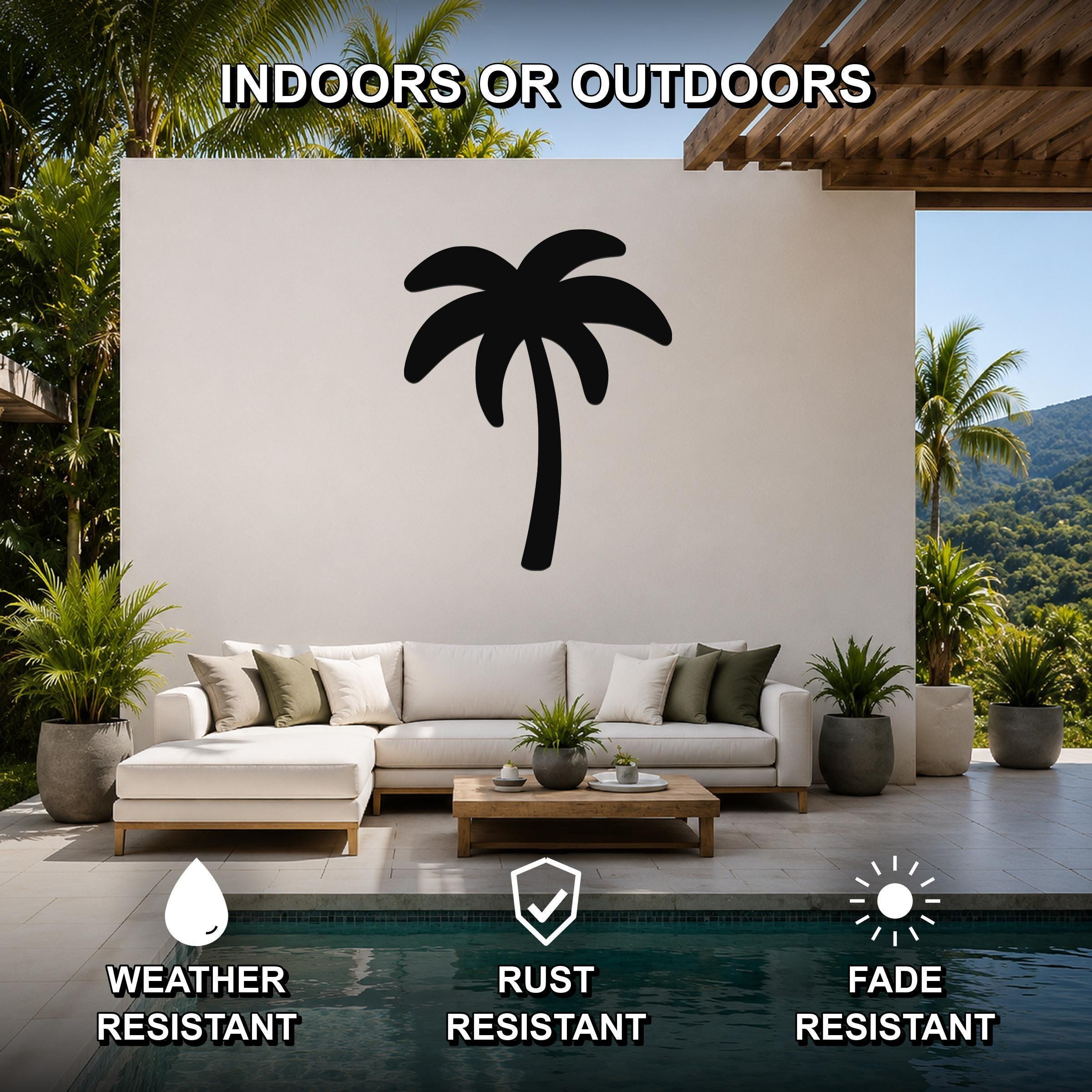 Black metal palm tree wall art silhouette mounted on a white outdoor wall above a white sectional sofa in a tropical patio setting.