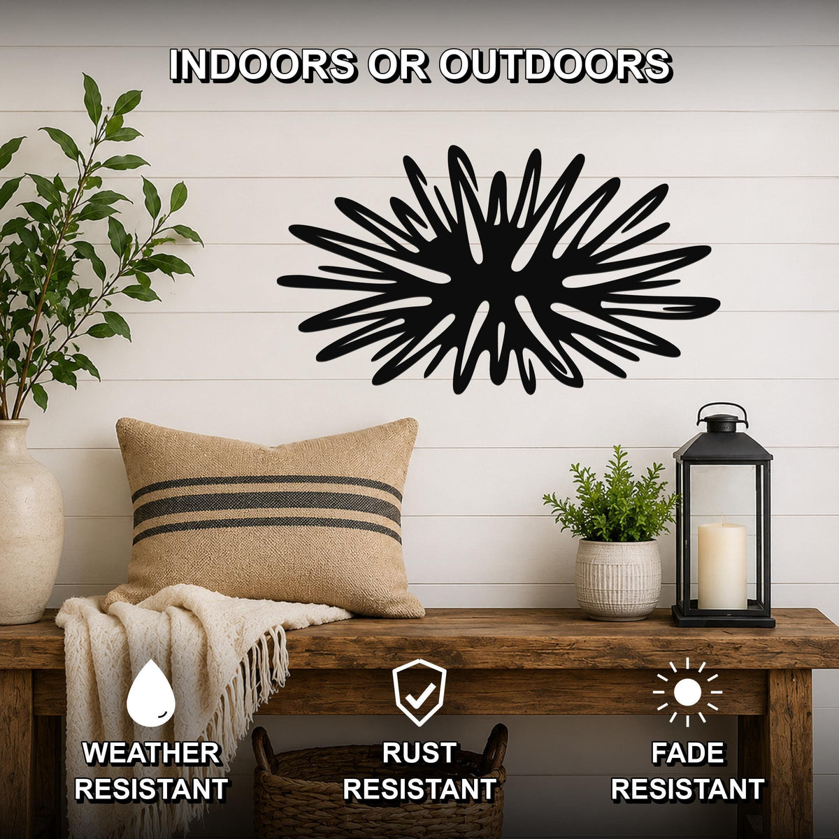 Black metal sea urchin wall art with spiky cutout rays, mounted on a white shiplap wall above a wooden bench in a living room.
