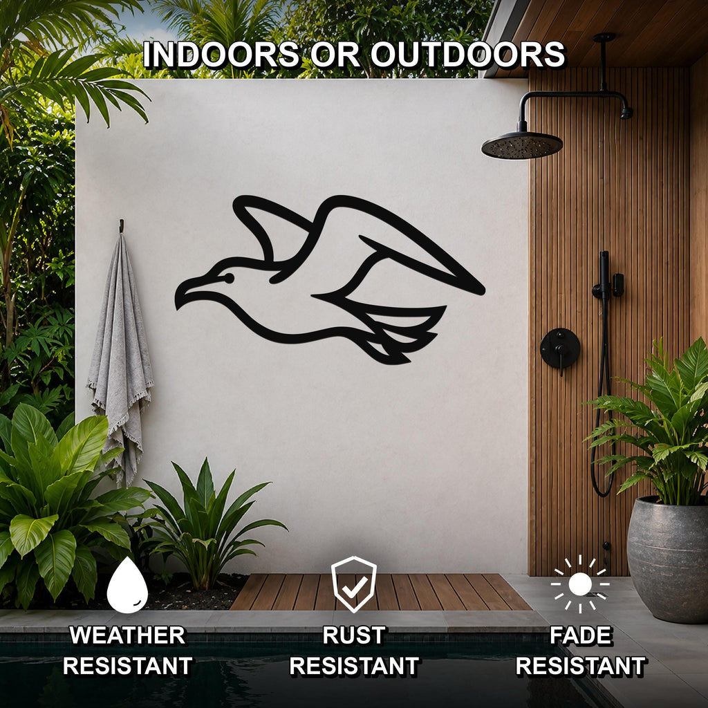 Black metal seagull wall art with motion-line cutouts, mounted on a white outdoor shower wall beside a wooden slat panel and potted plants.
