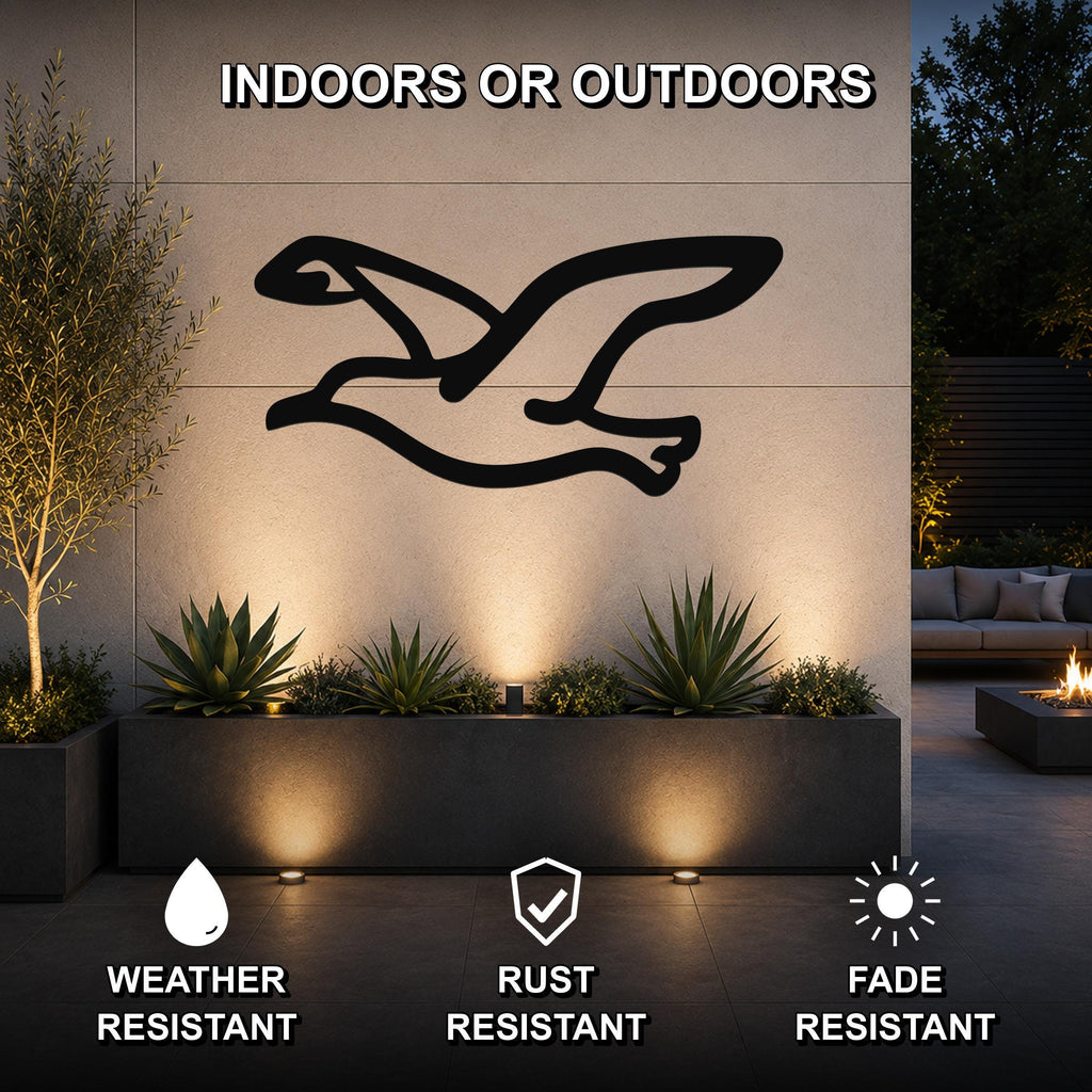 Black metal seagull wall art with a silhouette design, mounted on an outdoor wall above a planter in a patio setting.