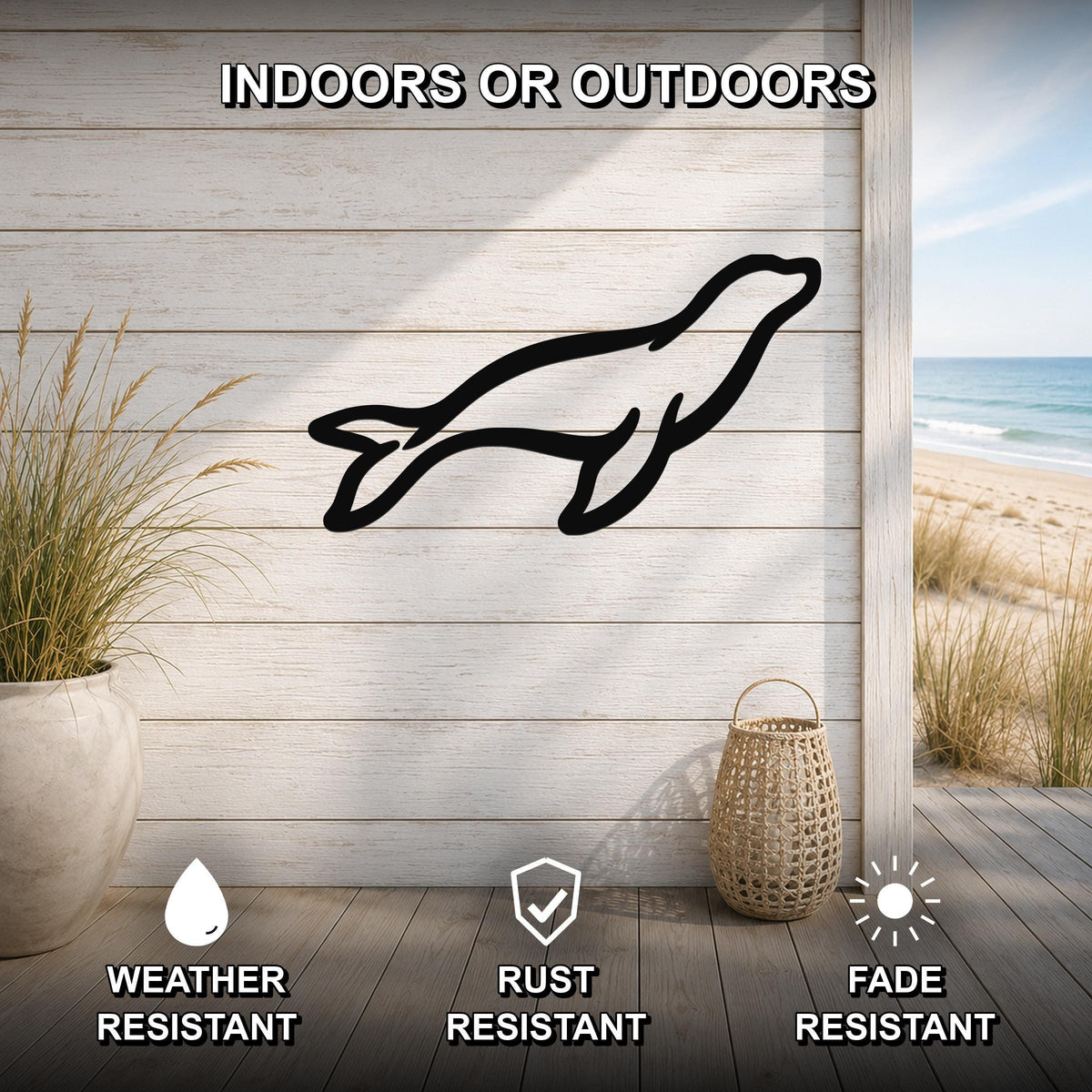 Black metal sea lion silhouette wall art mounted on a light wood plank wall, shown in an indoor-outdoor setting with a beach view, weather resistant, rust resistant, and fade resistant.